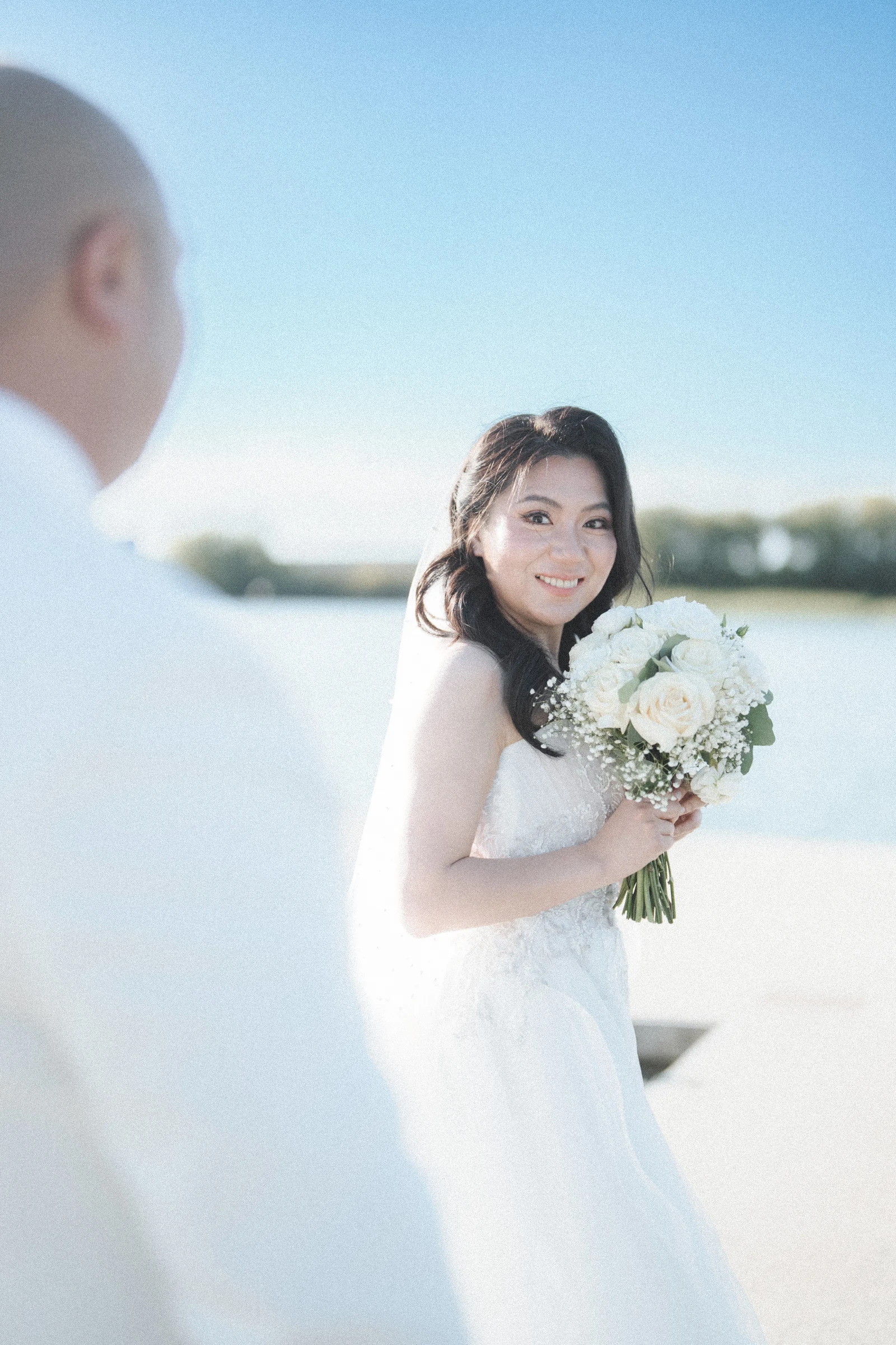 Bride looking back towards the groom beside the bright waterfront.