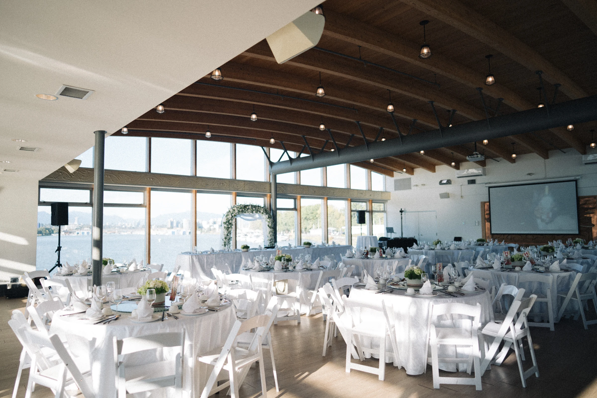 Reception tables and white chairs beneath the timber ceiling at UBC Boathouse.