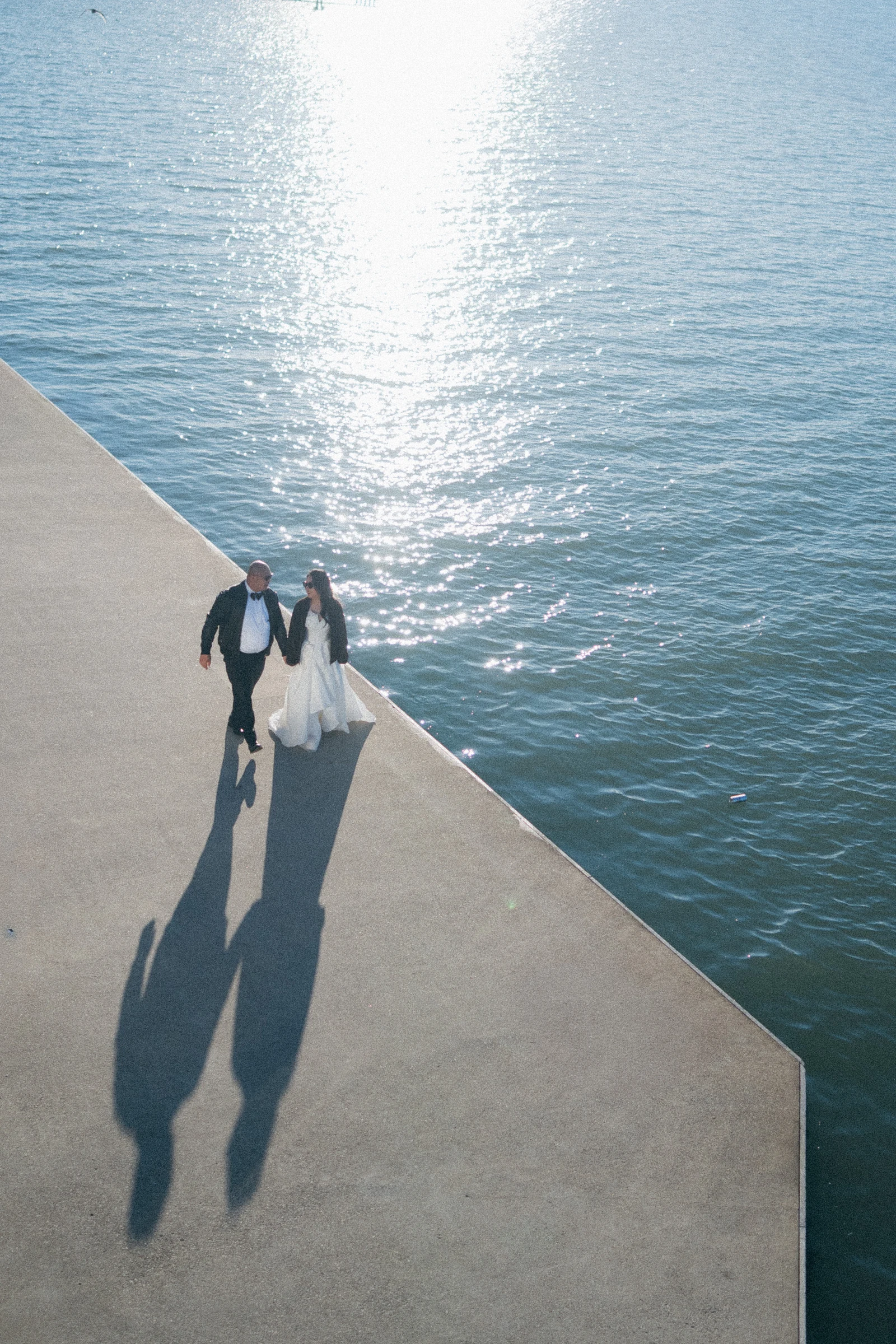 Overhead view of the couple casting long shadows across the waterfront deck.