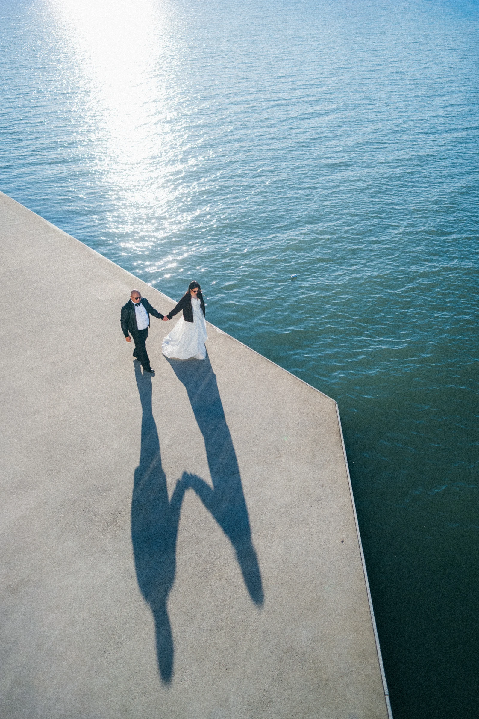 Couple lifting their joined hands, photographed from above beside the water.