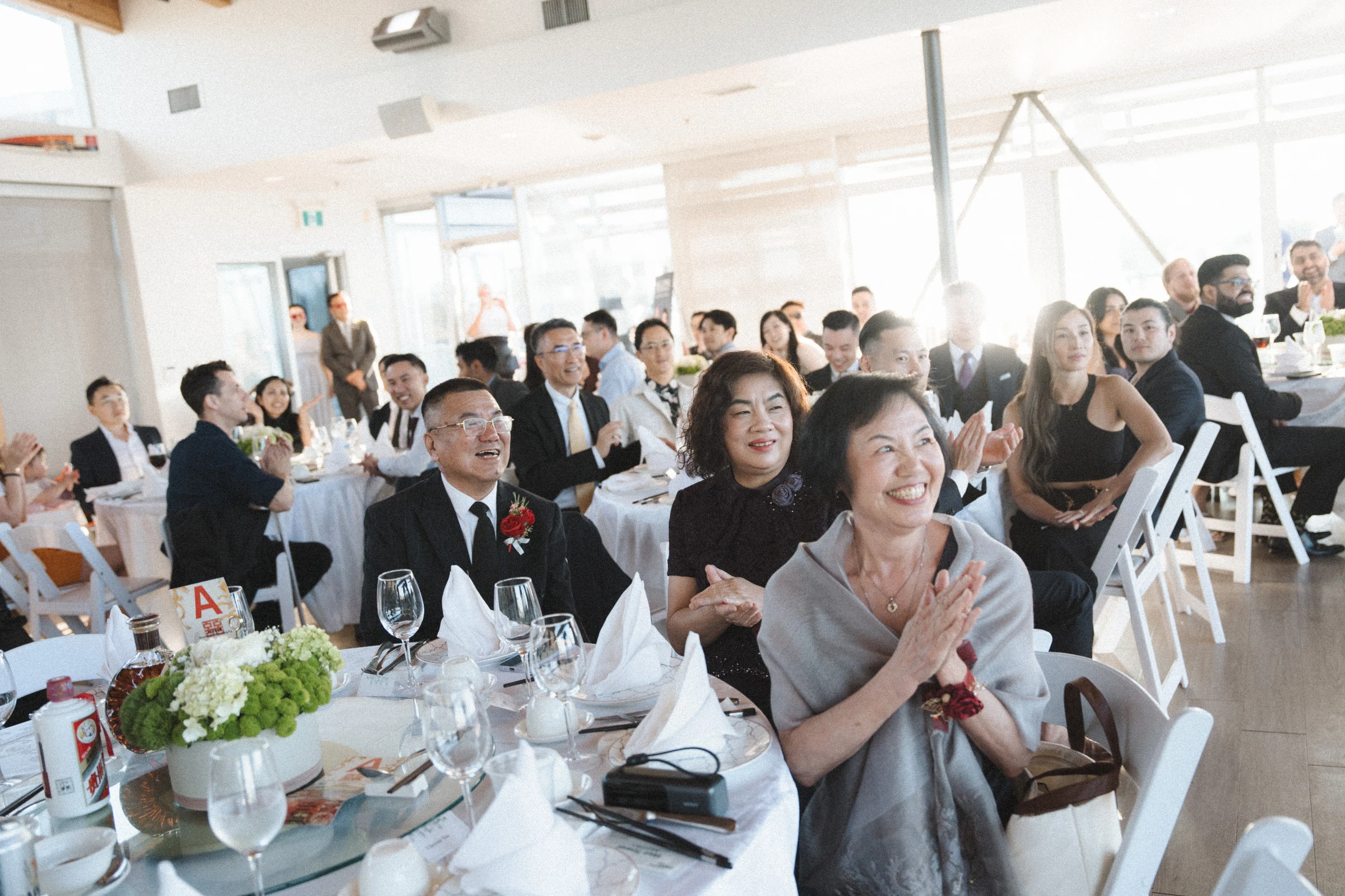 Reception guests applauding from tables inside the boathouse.