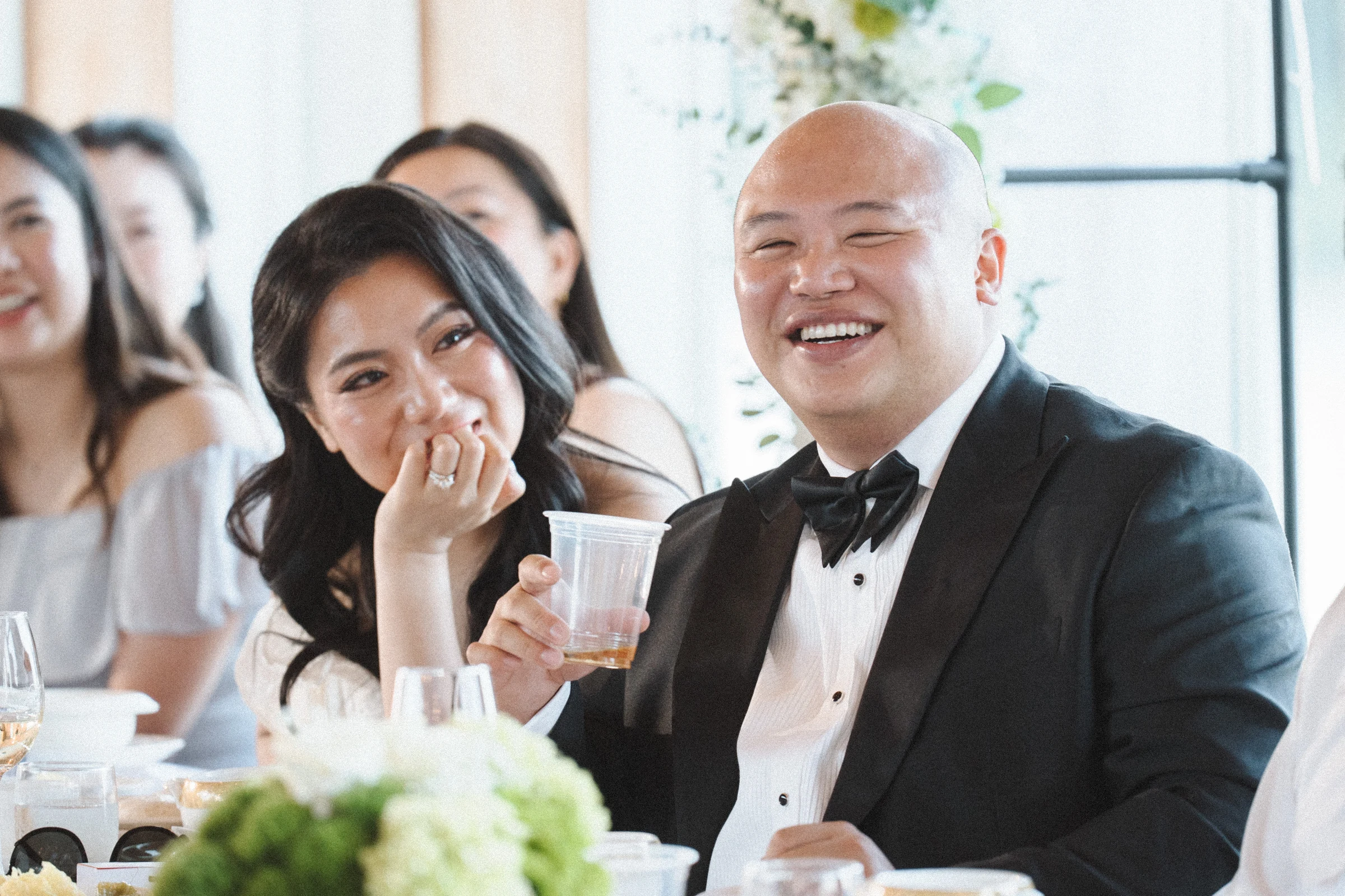 Bride covering her mouth as the groom laughs beside her during the speeches.