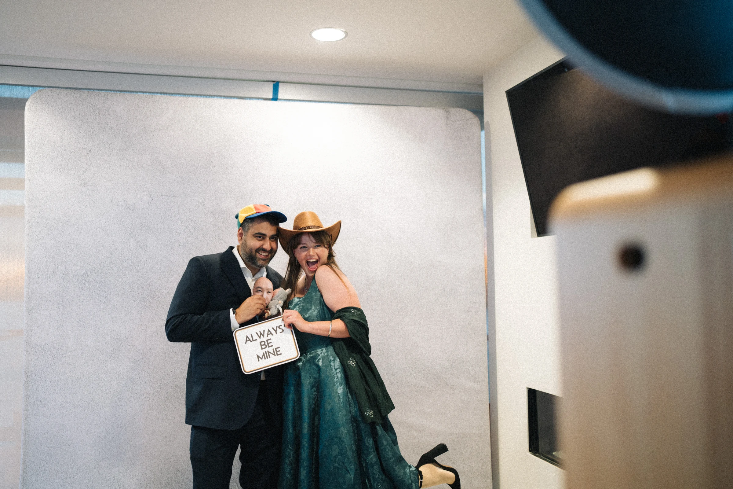 Two guests posing together against a plain reception wall.