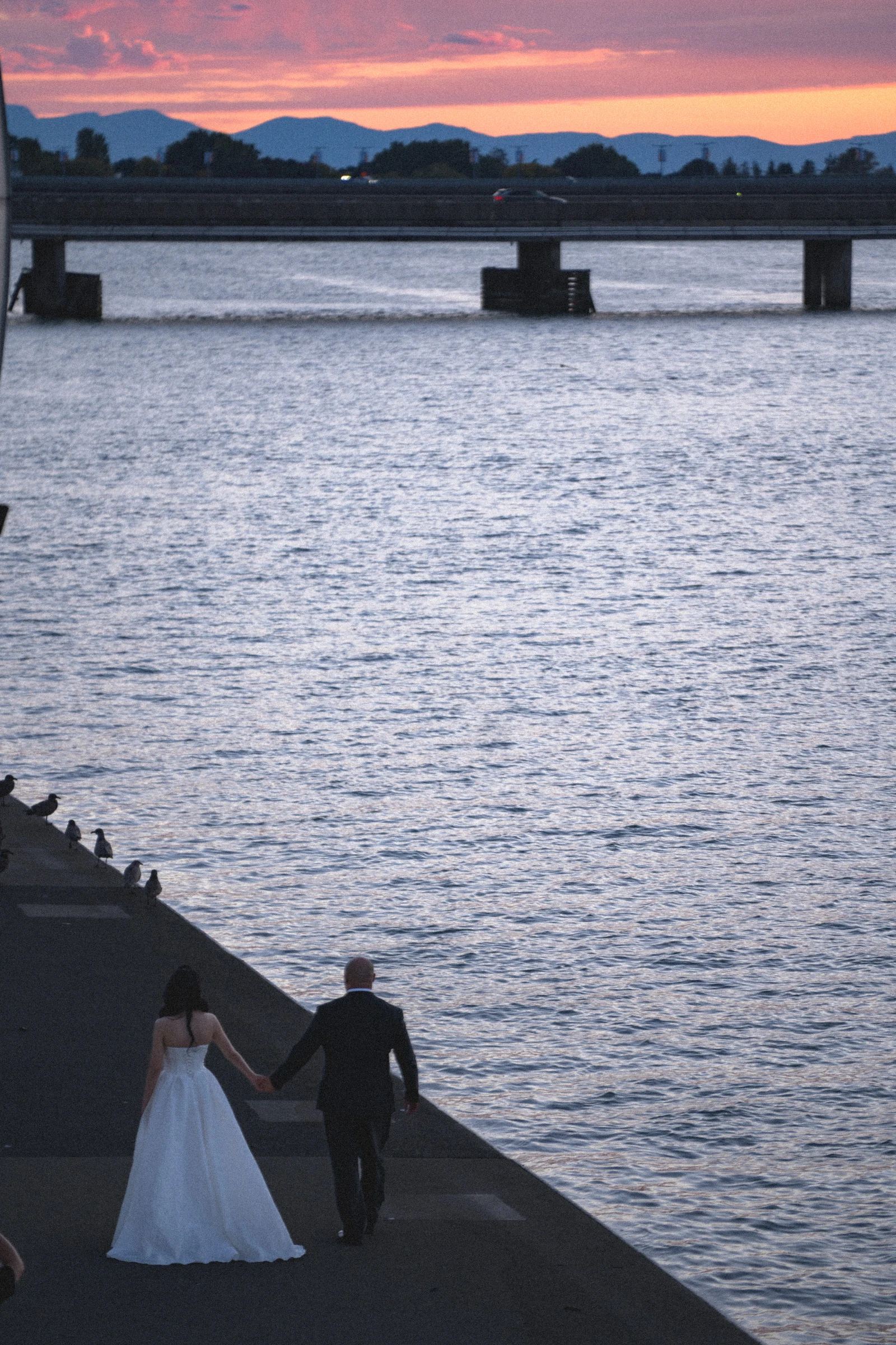 Elevated view of the couple near the end of the waterfront deck at dusk.