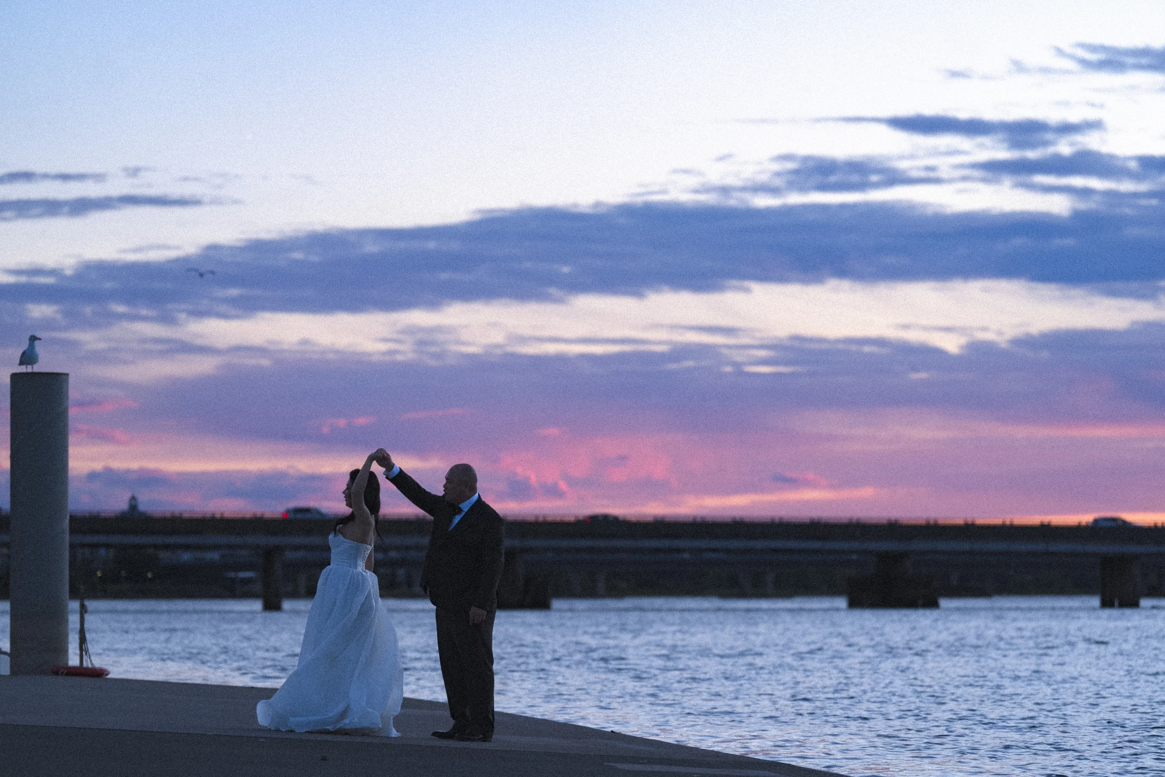 Couple turning together beneath the pink magic-hour sky.