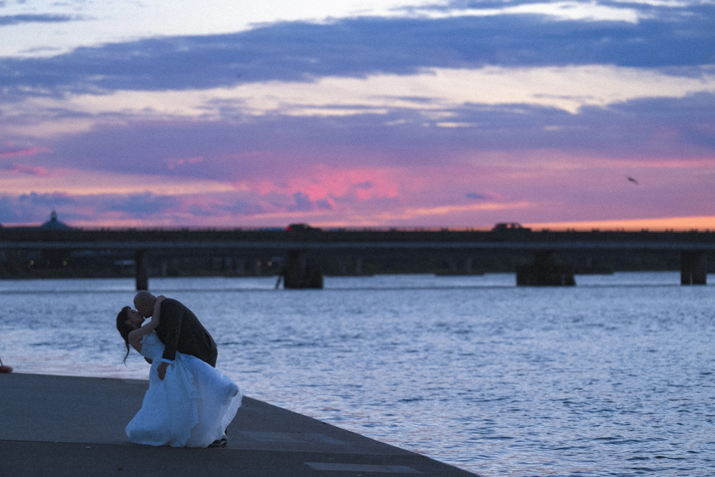 Bride and groom holding each other beneath a band of pink cloud.