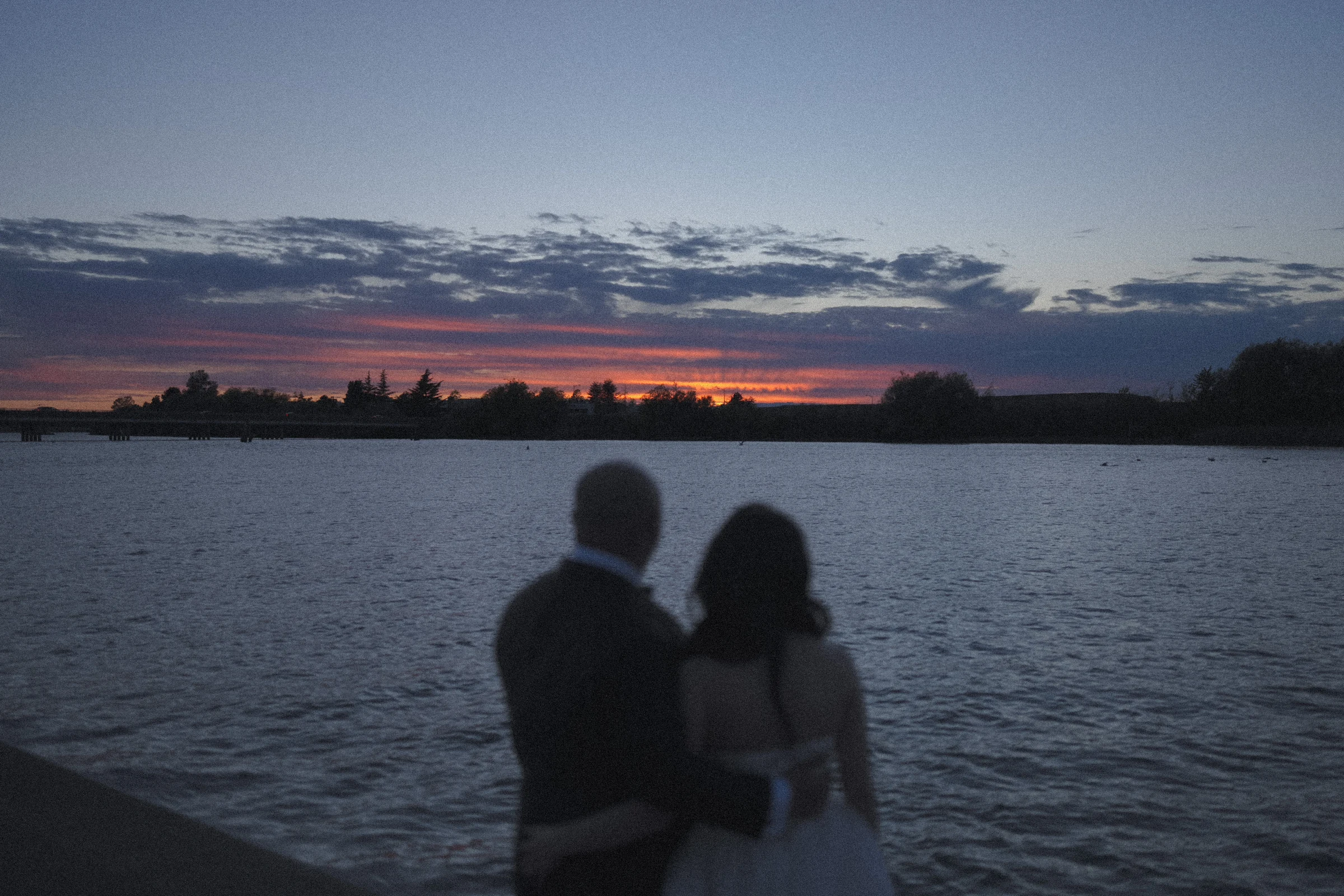 Softly focused silhouette of the couple facing the river at dusk.