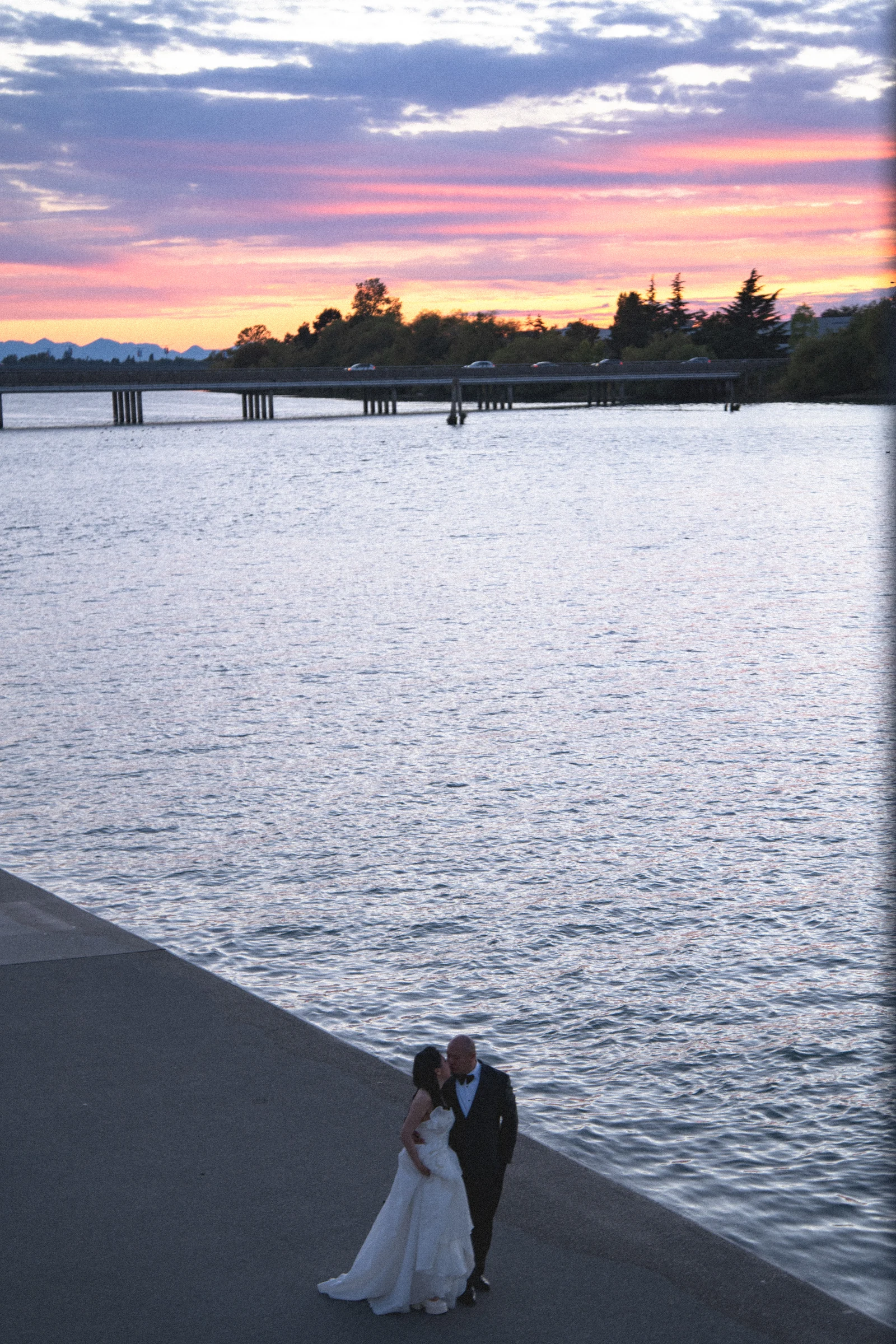 Tall portrait of the couple beneath the last pink light over the river.