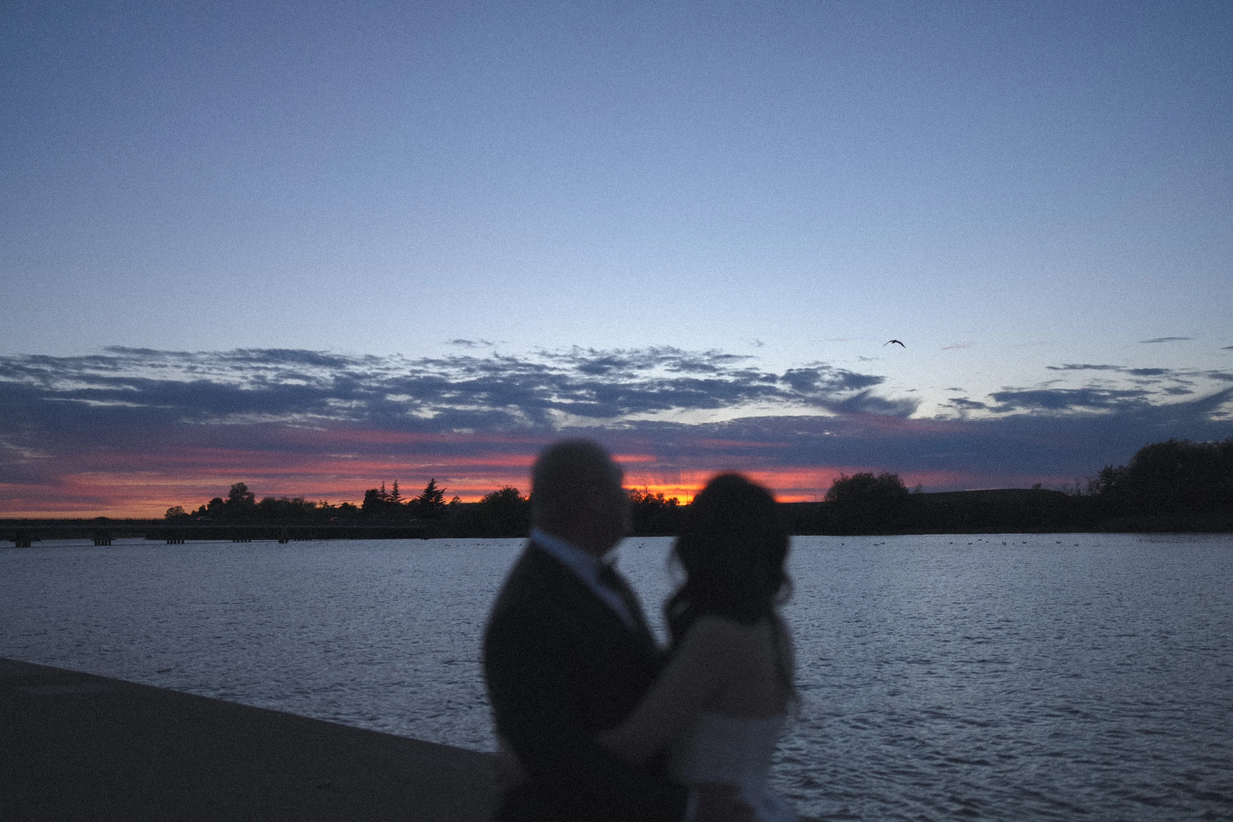 Soft silhouette of the couple leaning close beneath the evening sky.