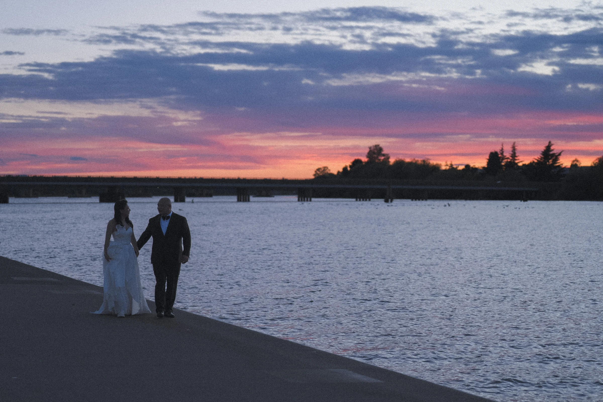 Wide view of the couple holding hands, with the pink horizon behind them.