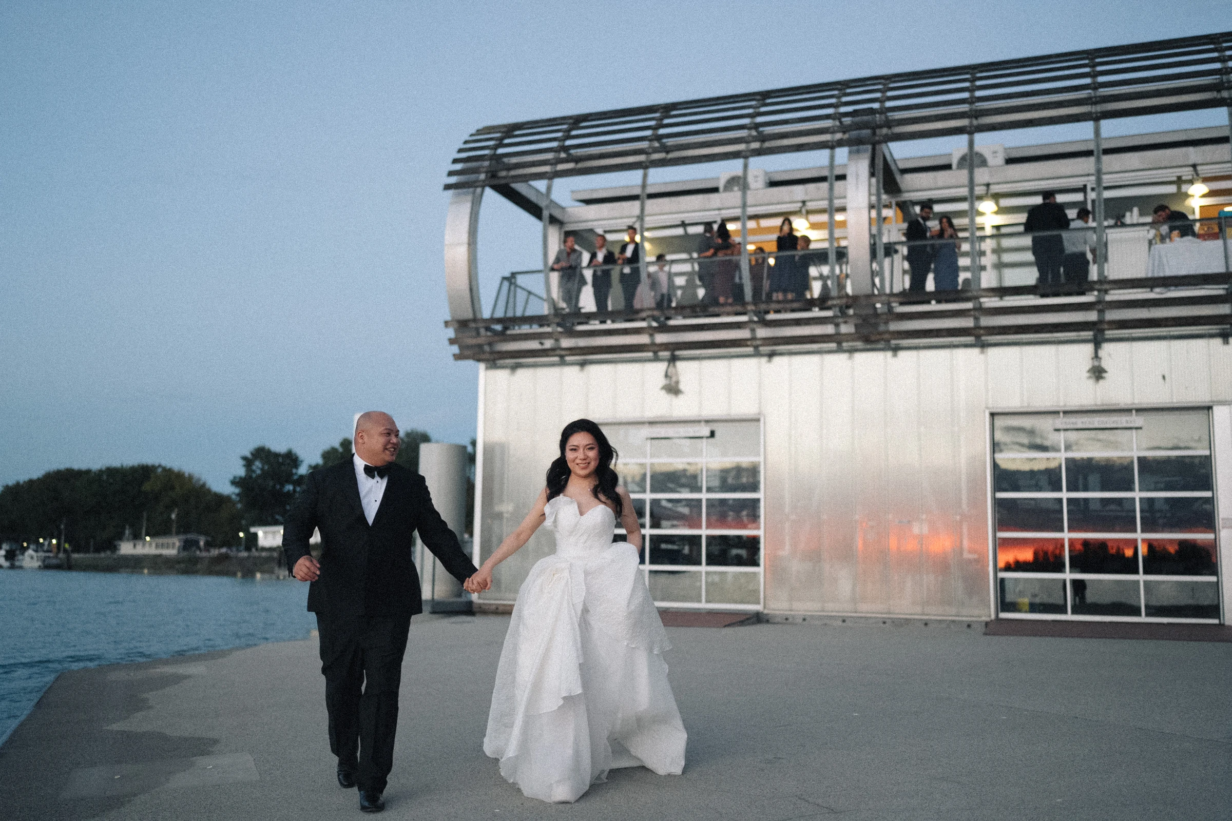 Couple walking beside the lit boathouse as evening falls.