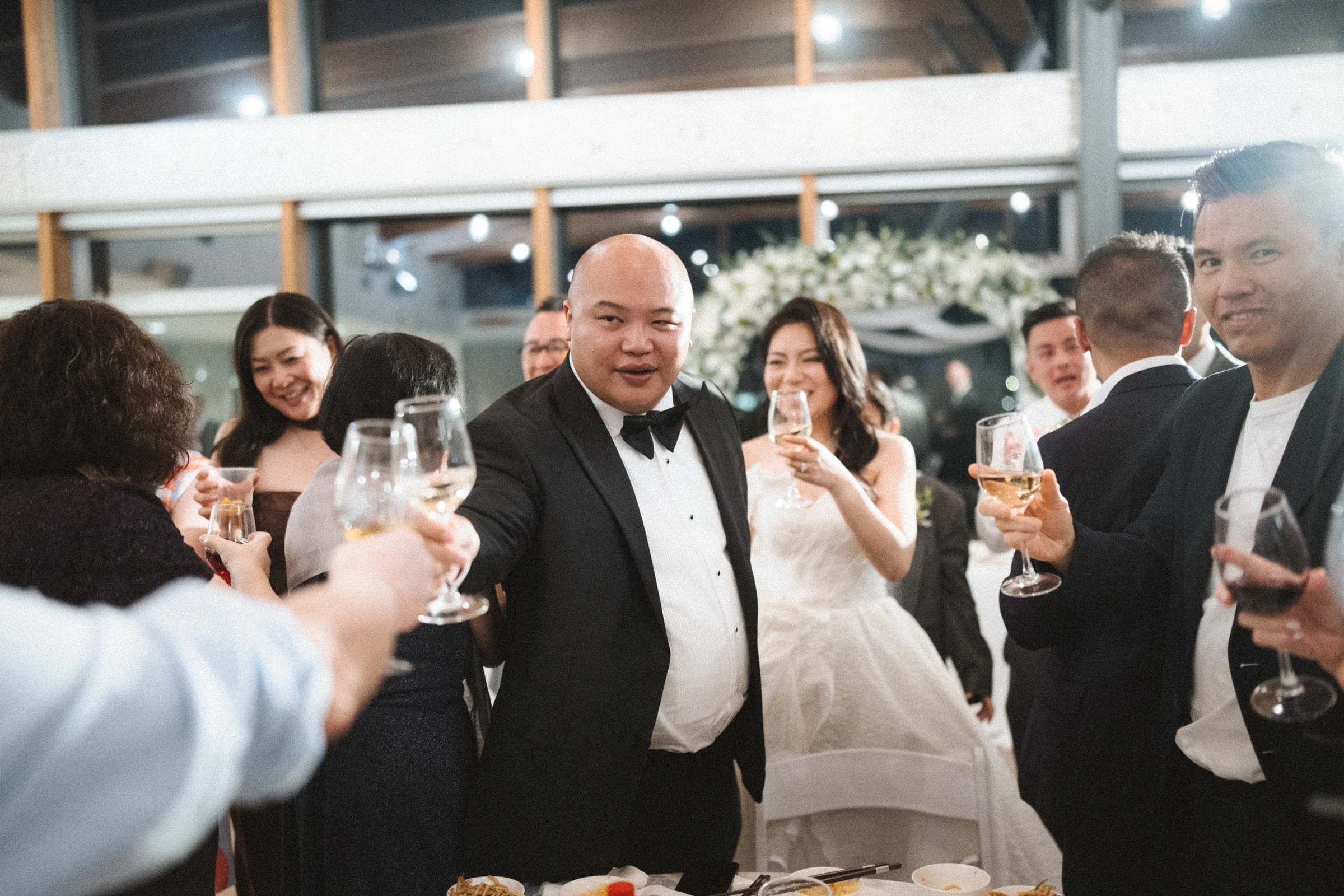 Couple raising glasses with guests beside the reception tables.