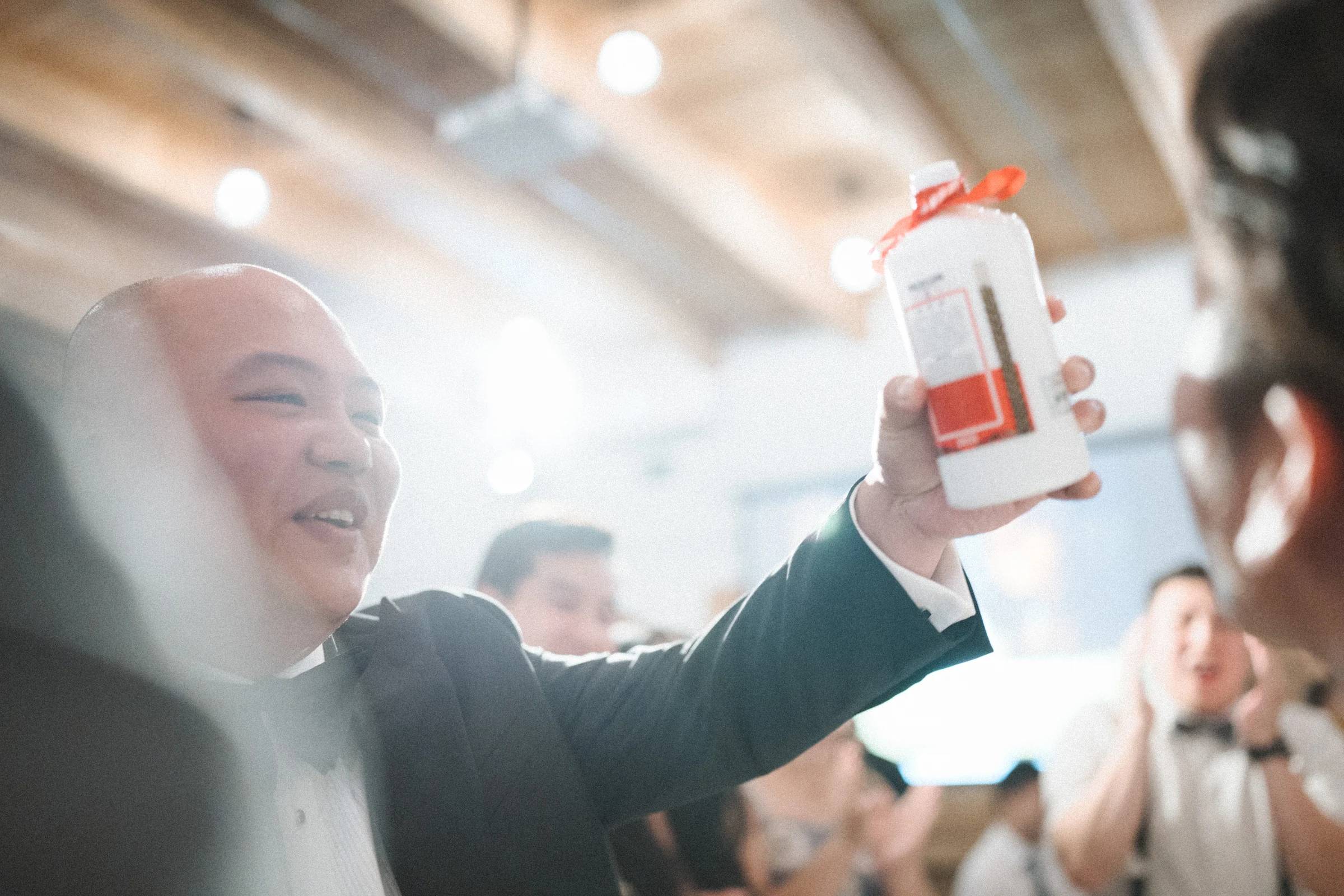 Guest lifting a drink towards the camera beneath the reception lights.