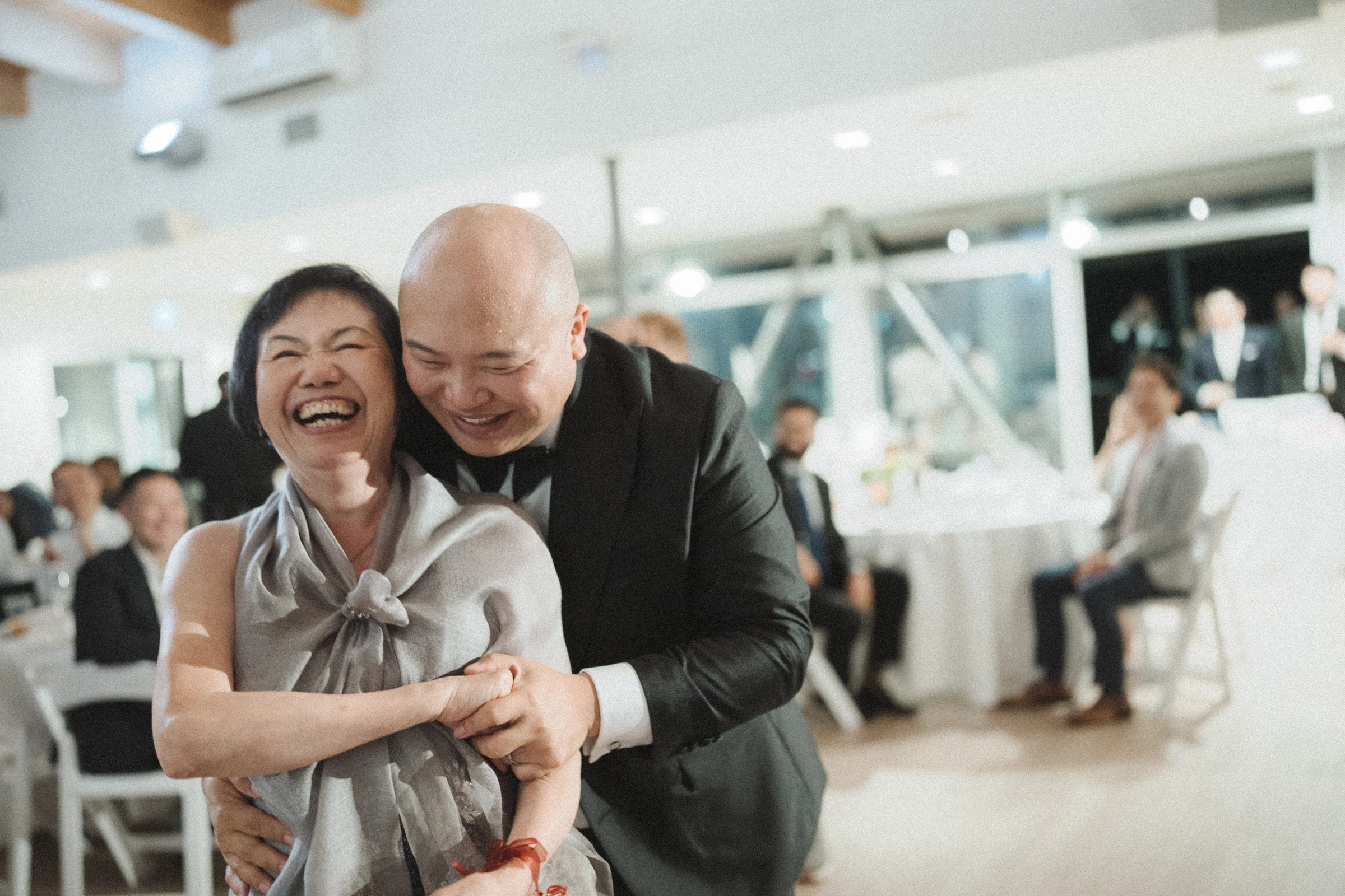 Bride and groom sharing a laughing embrace with a guest.