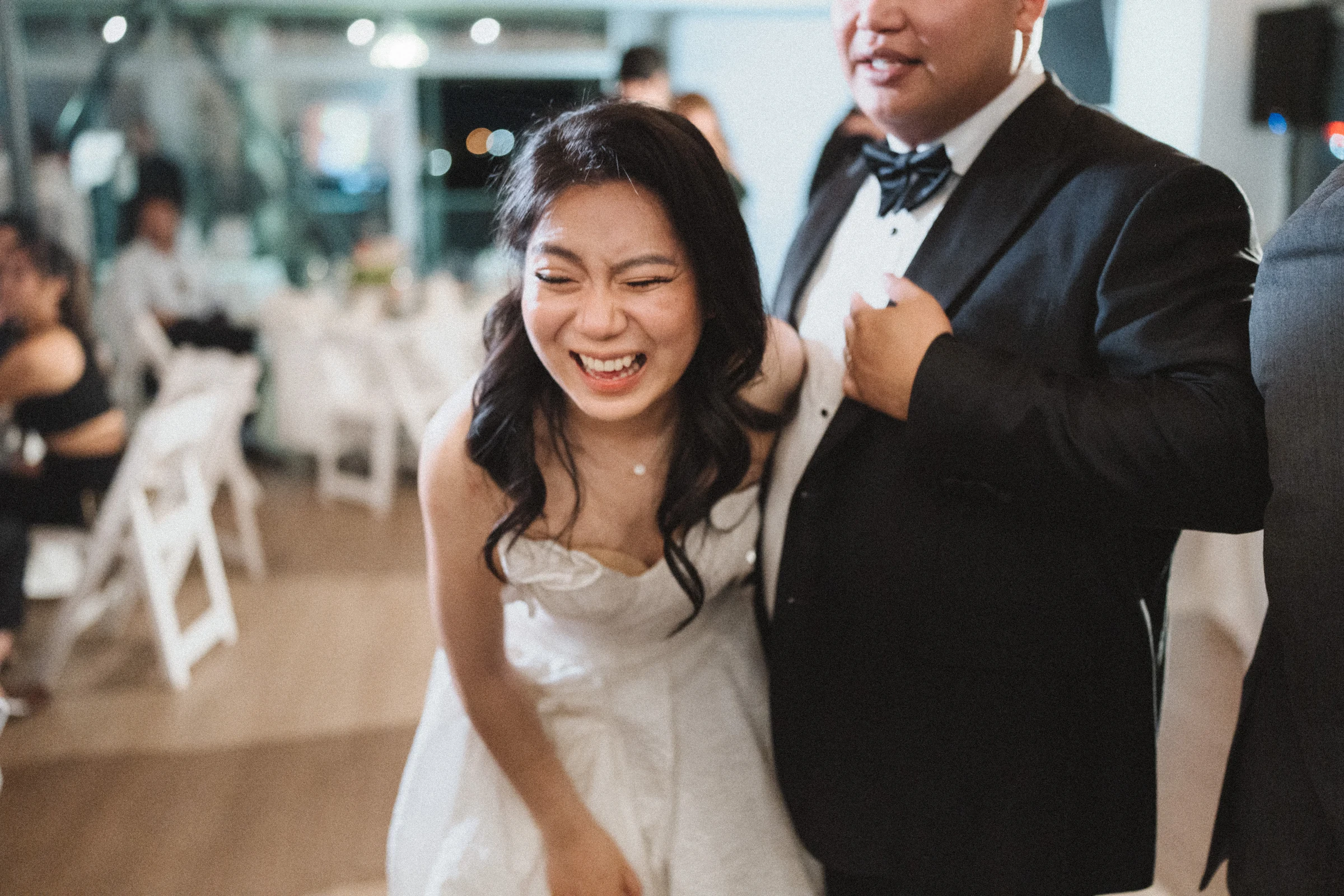 Bride laughing as the groom stands close behind her on the dance floor.