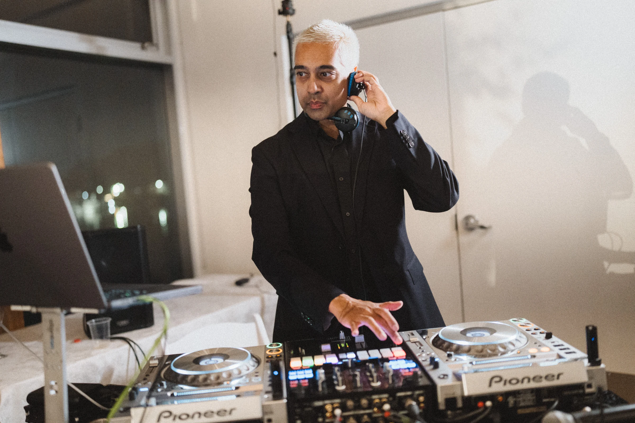 DJ working behind the reception decks with one hand near his headphones.