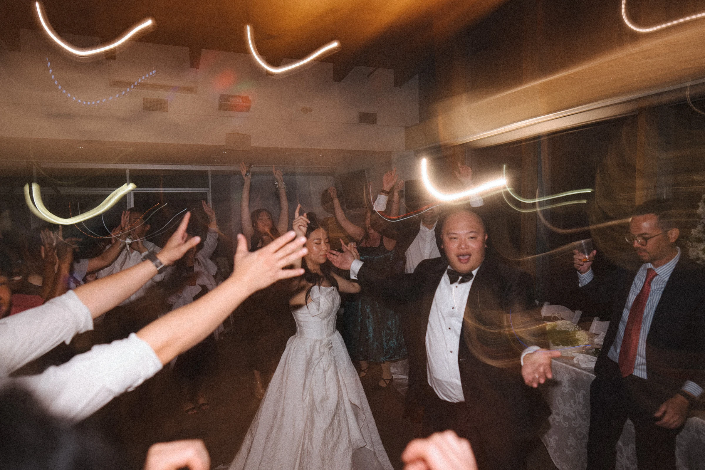 Couple dancing among raised hands and trails of warm light.