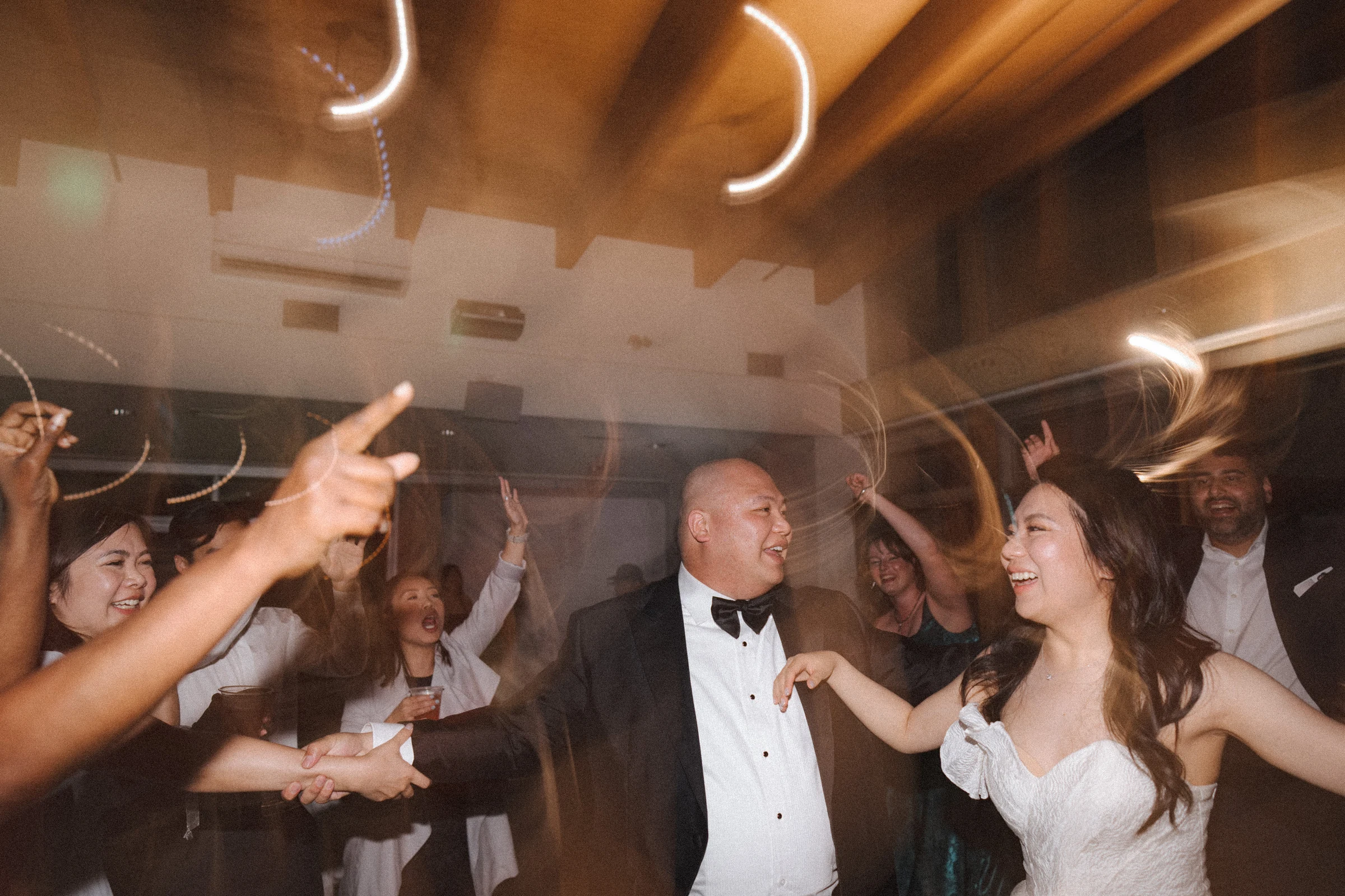 Bride and groom smiling towards each other on the crowded dance floor.