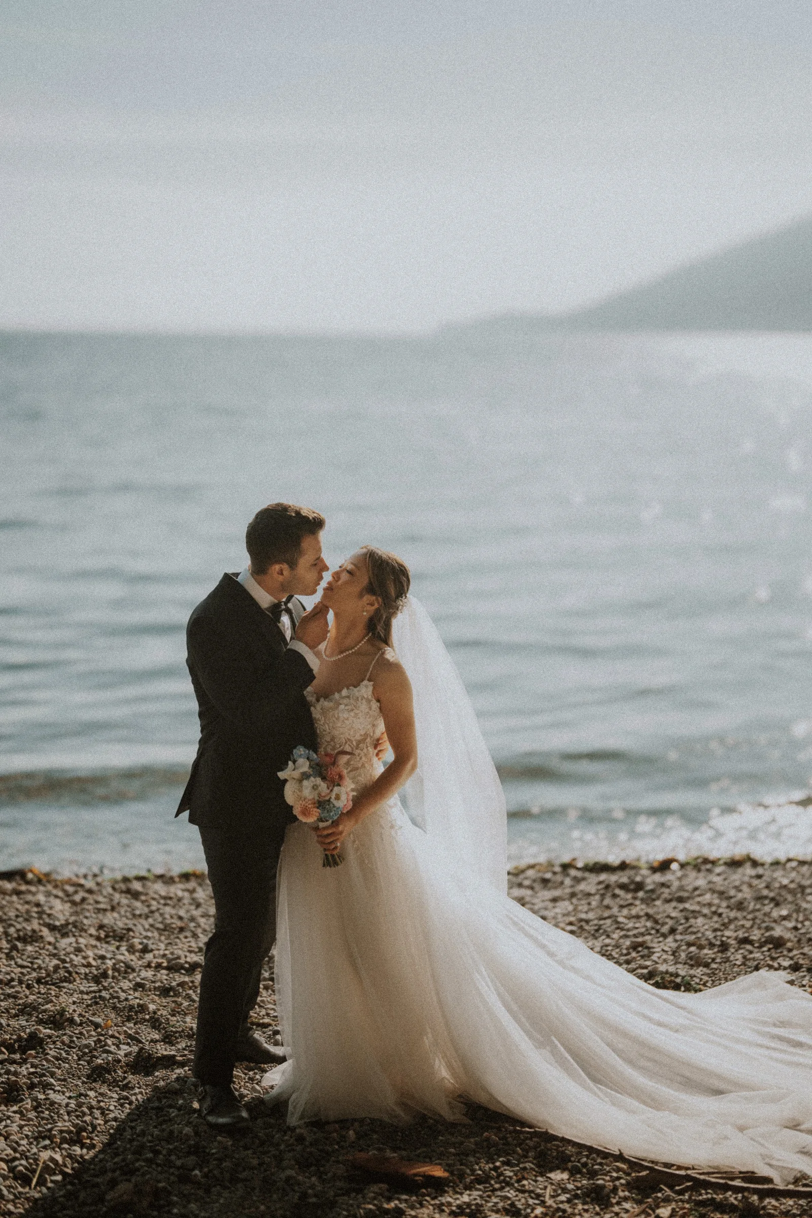 Couple kissing on the pebbled shoreline at Whytecliff Park.