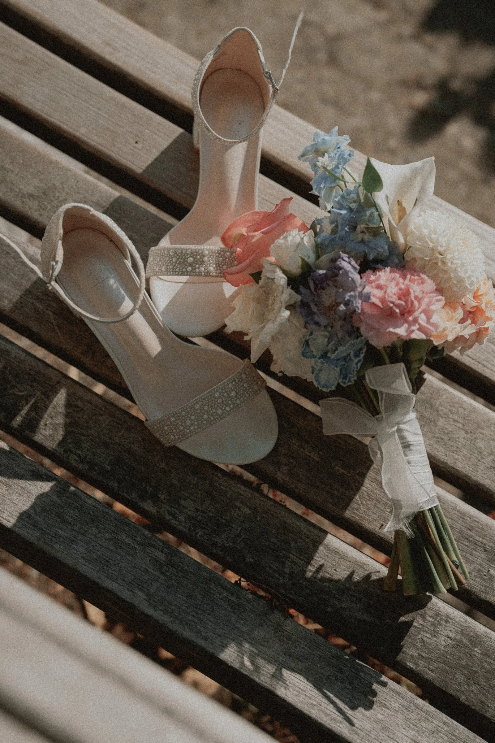 Bridal shoes and a pink-and-white bouquet arranged on a wooden bench.