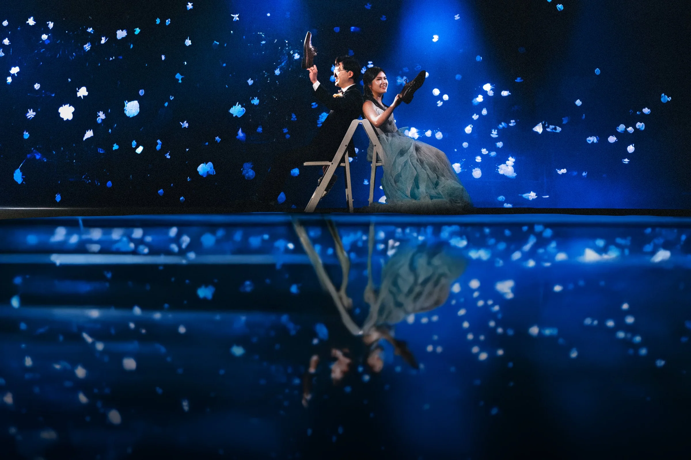 Couple playing the shoe game on stage, dramatic blue lighting, Vancouver Aquarium reception.