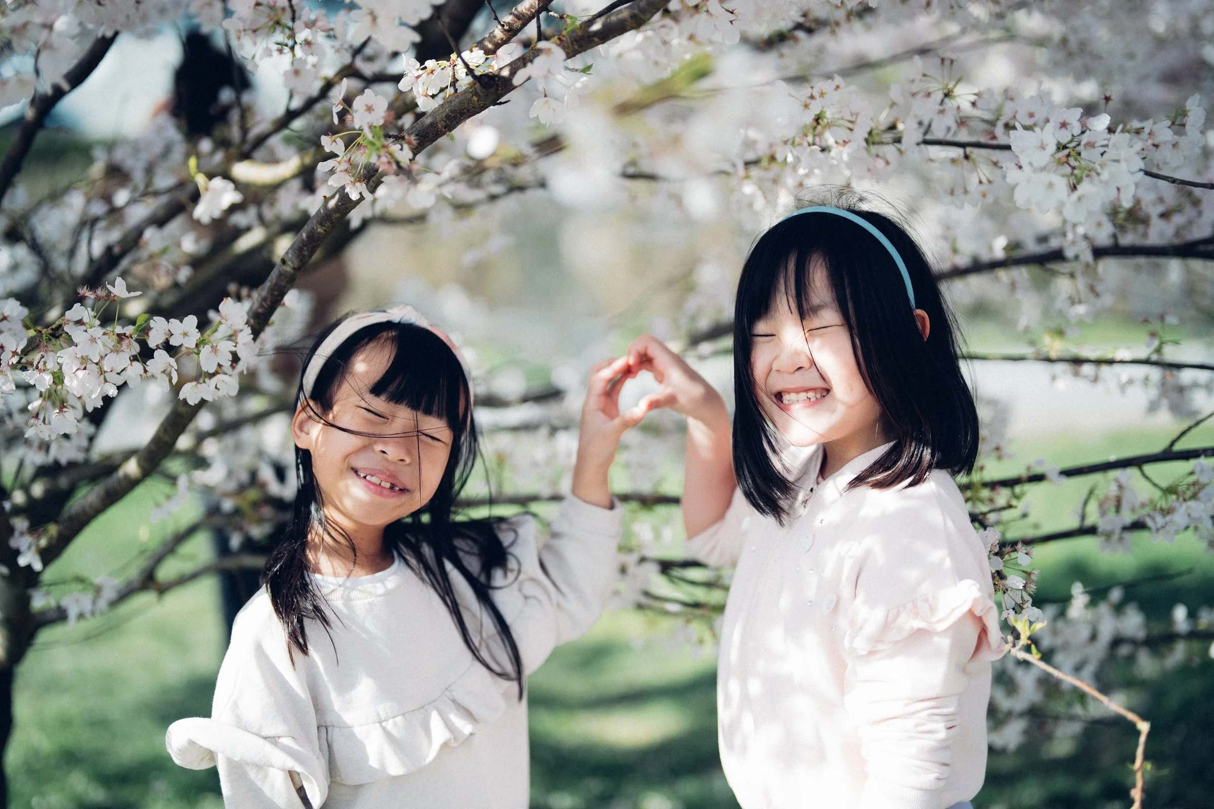 Two smiling children beneath flowering cherry blossom branches.