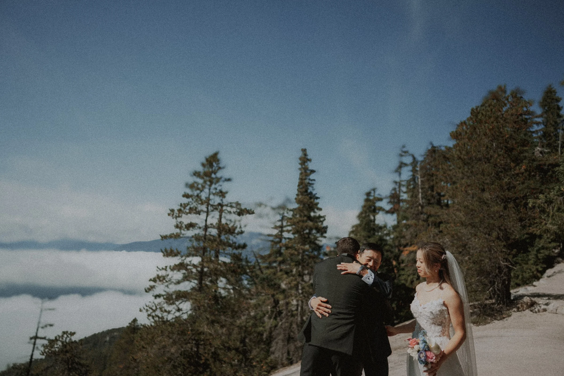 Bride watching as the groom embraces her accompanying guest.