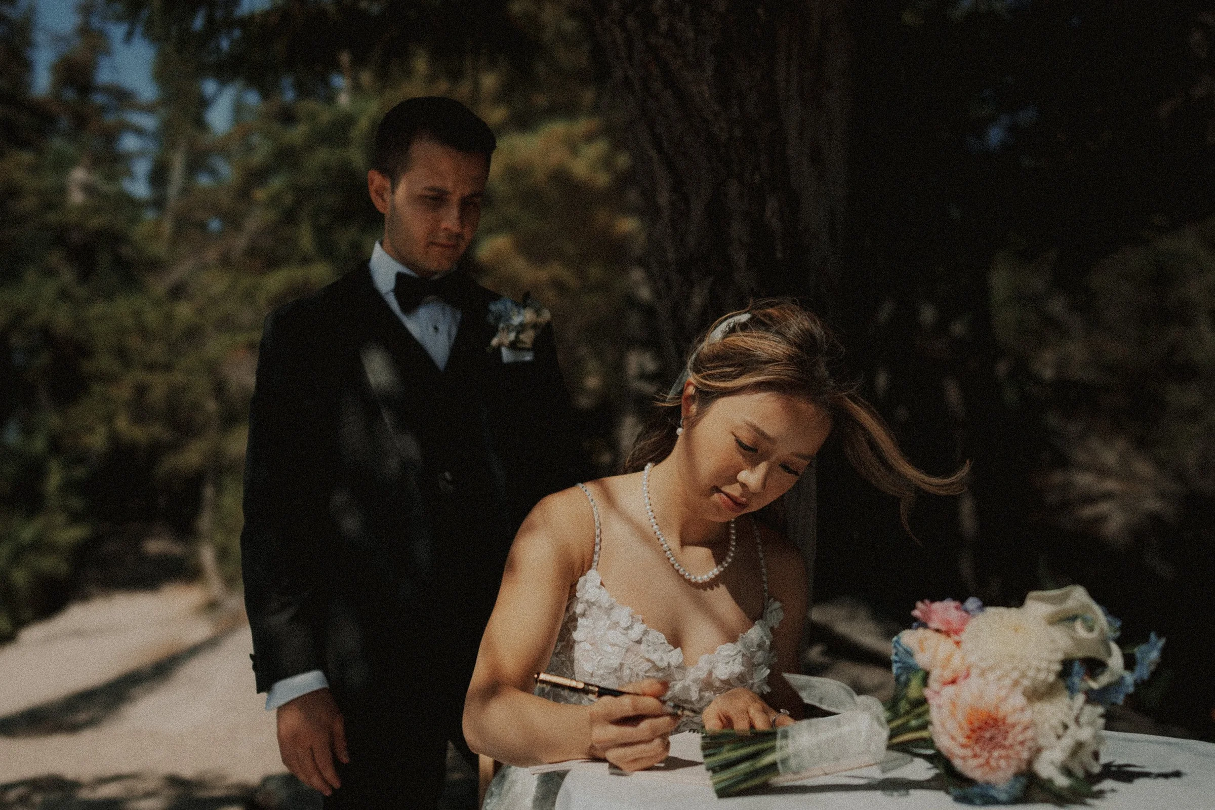 Bride signing marriage license, groom watching, candid wedding portrait.