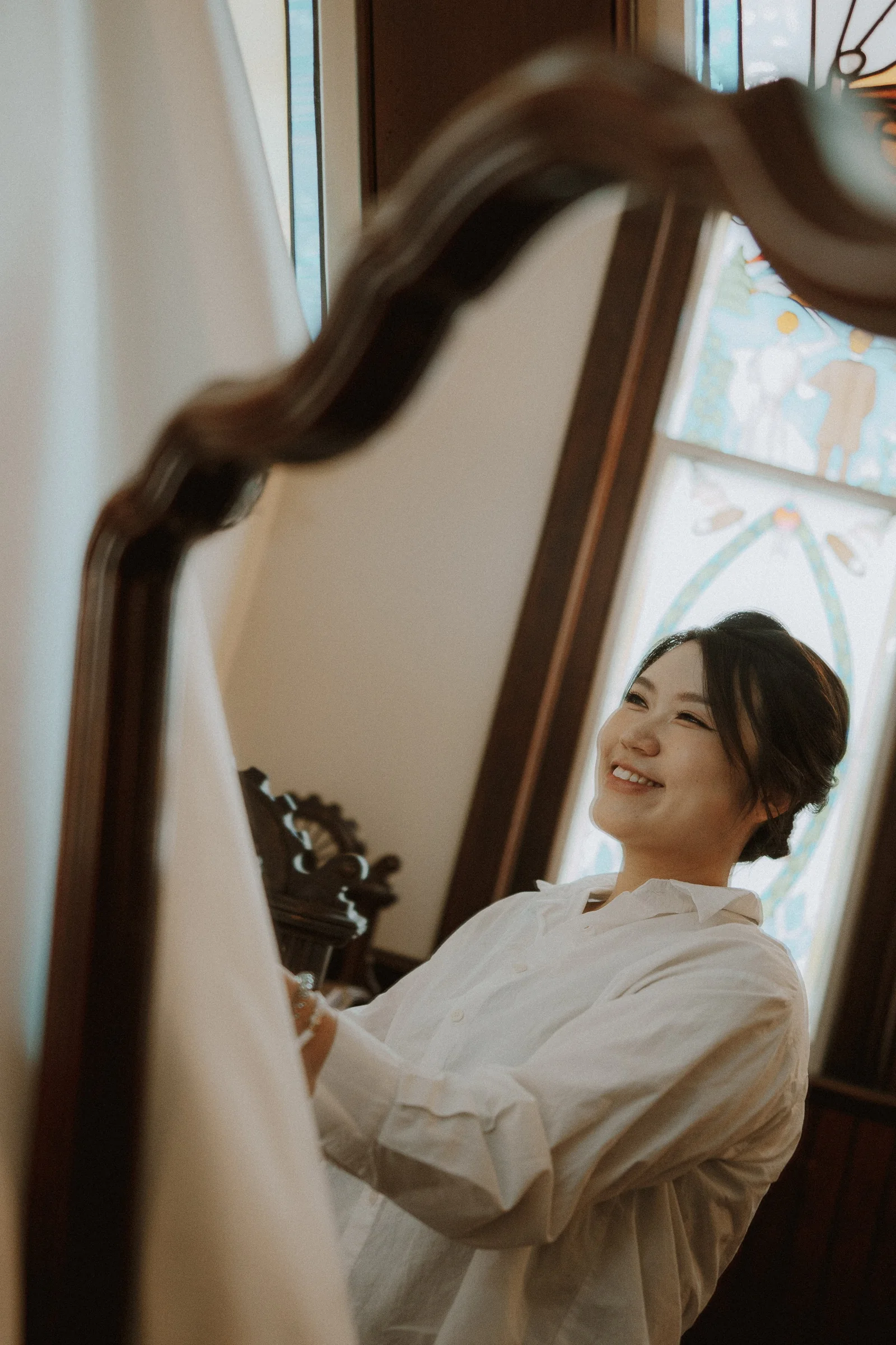 Bride's reflection in a curved mirror while preparing beside a chapel window.