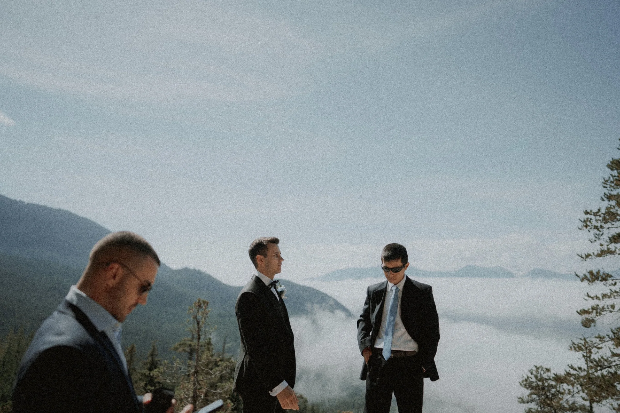 Groom and guests preparing for the ceremony above low mountain clouds.