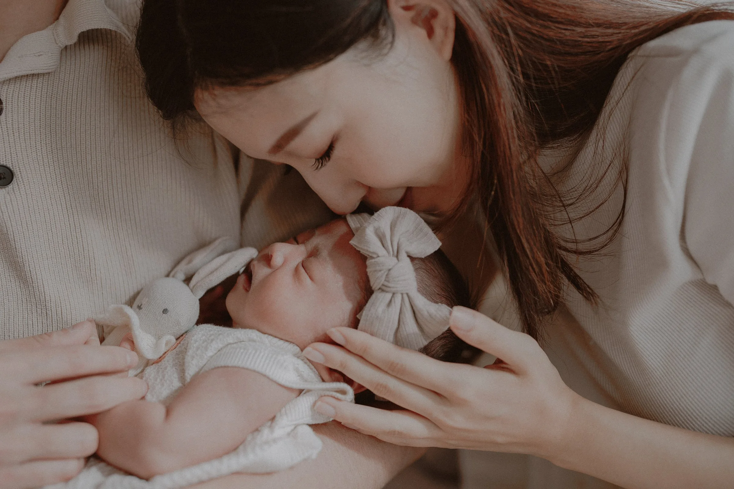 Parent kissing a newborn's forehead while gently cradling the baby's face.
