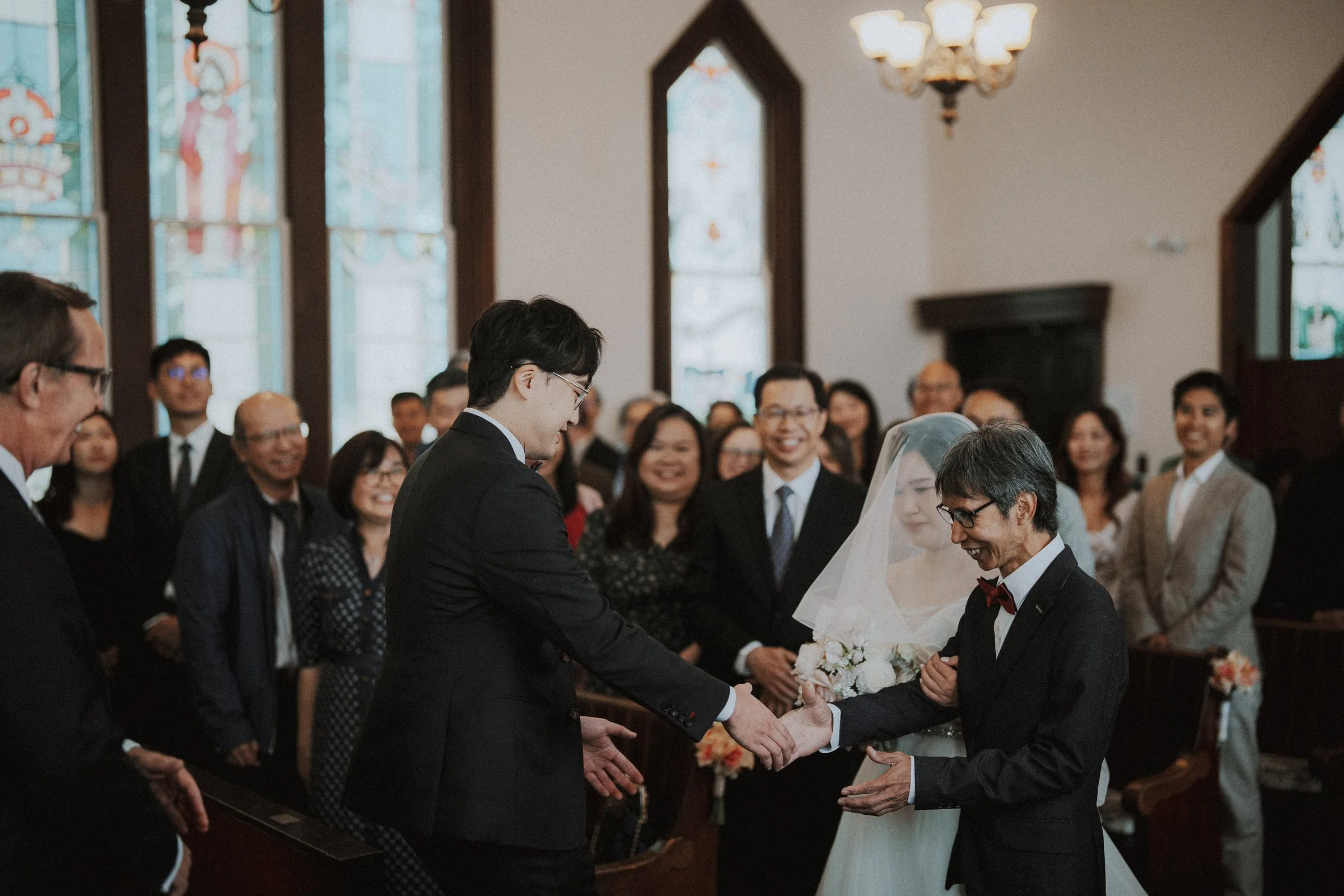 Groom shaking hands with a relative inside Minoru Chapel, guests in background.