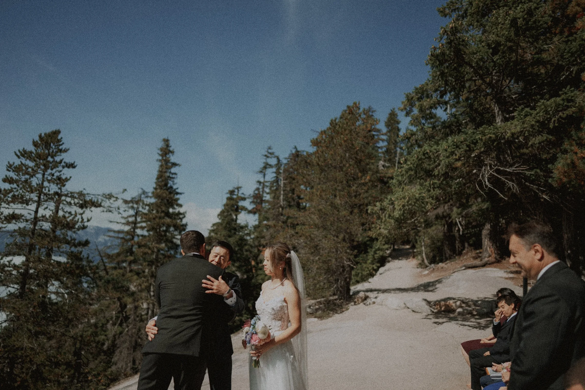 Groom greeting a guest beside the bride at the outdoor ceremony.