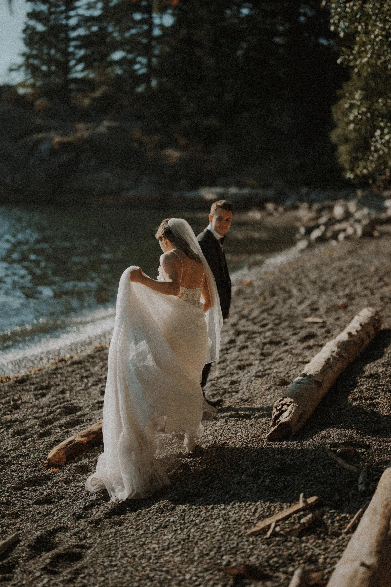 Bride lifting her gown as she walks along the beach beside the groom.