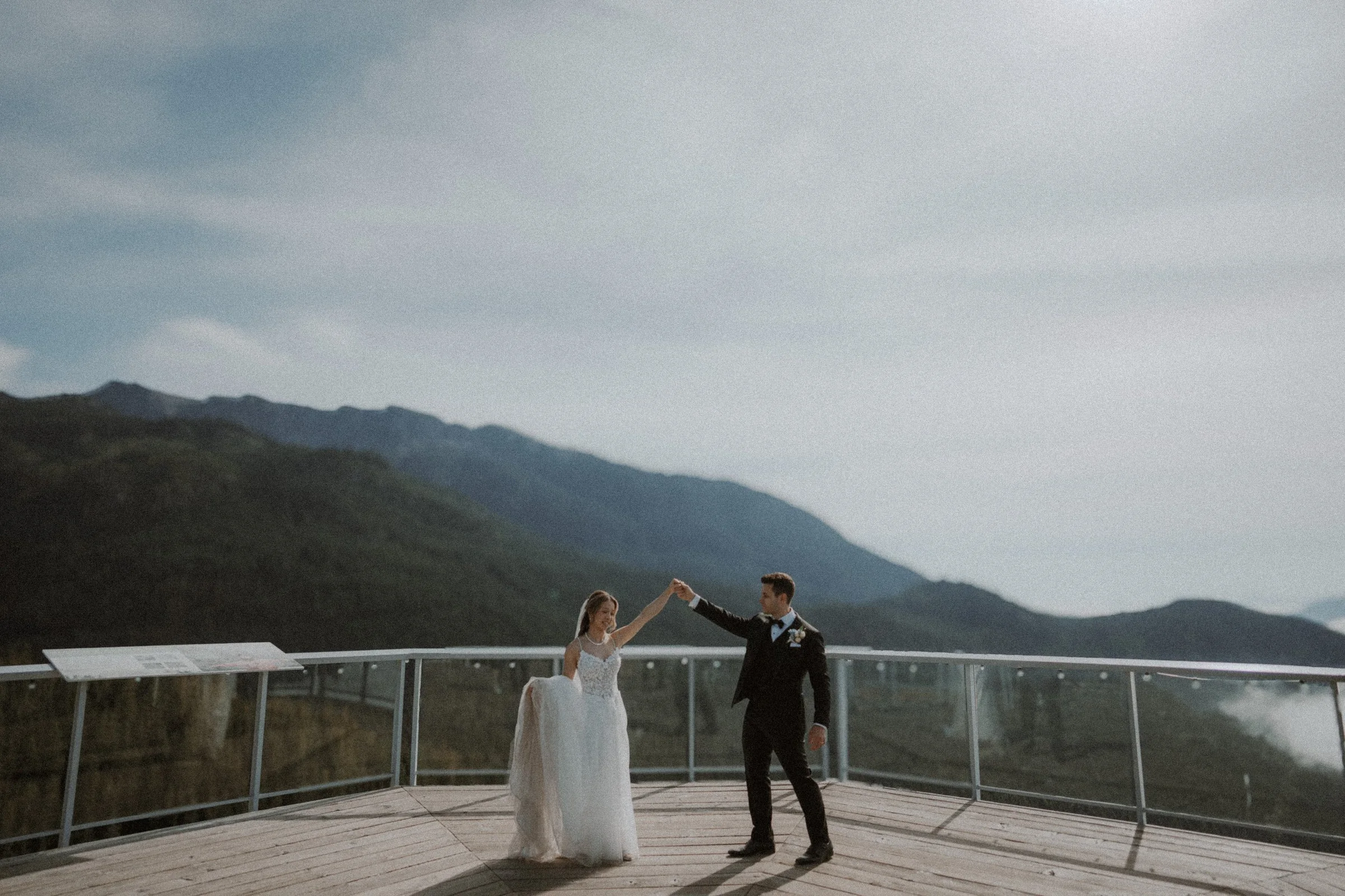 Groom twirling the bride on a timber deck overlooking the mountains.