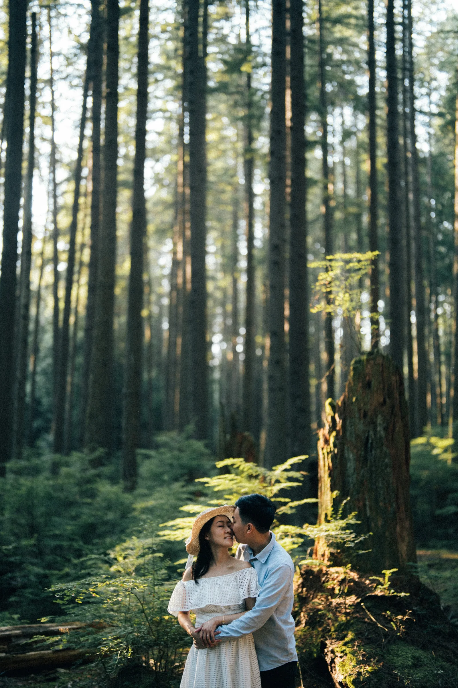 Intimate close-up of couple kissing under towering trees, Pacific Spirit Park.