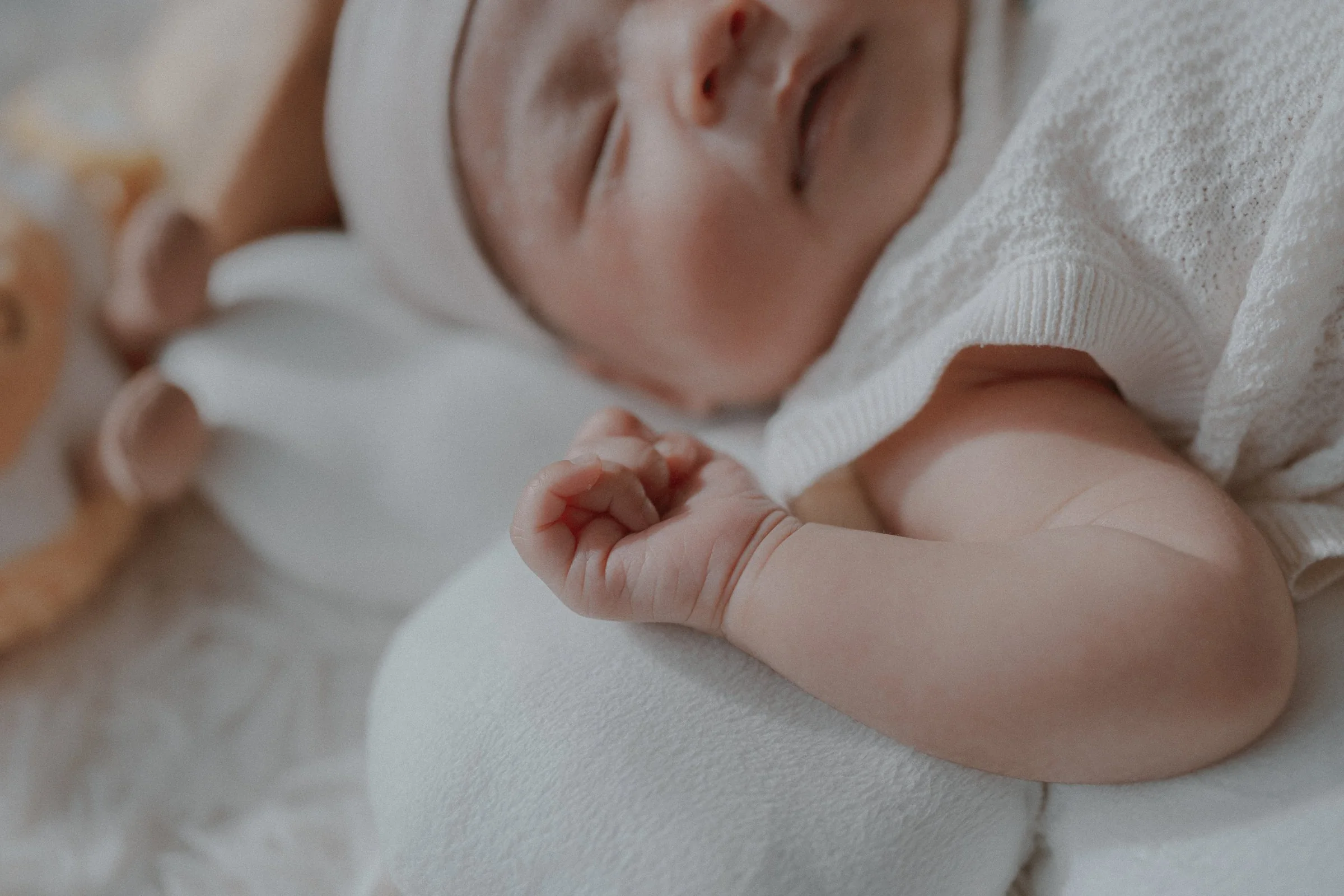 Detail of a newborn's curled hand beside a white knitted outfit.