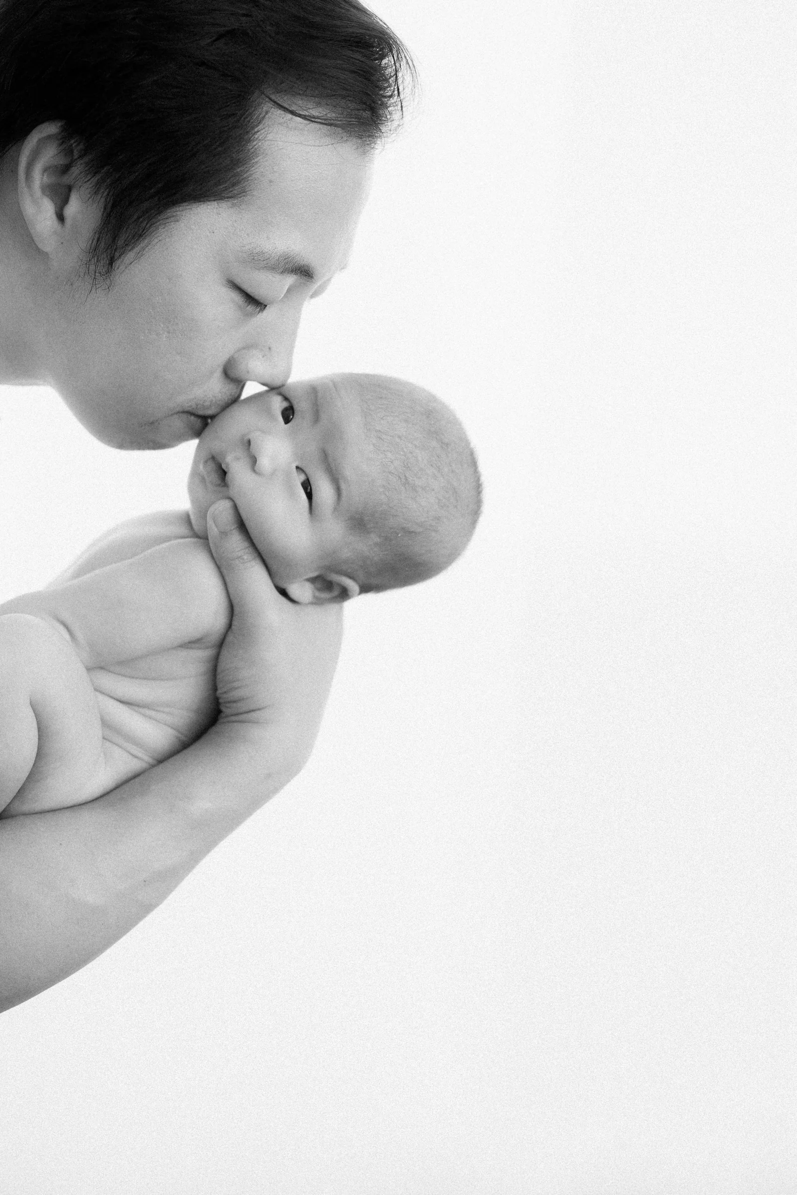 Father kissing newborn baby Apollo on the forehead, close-up portrait.