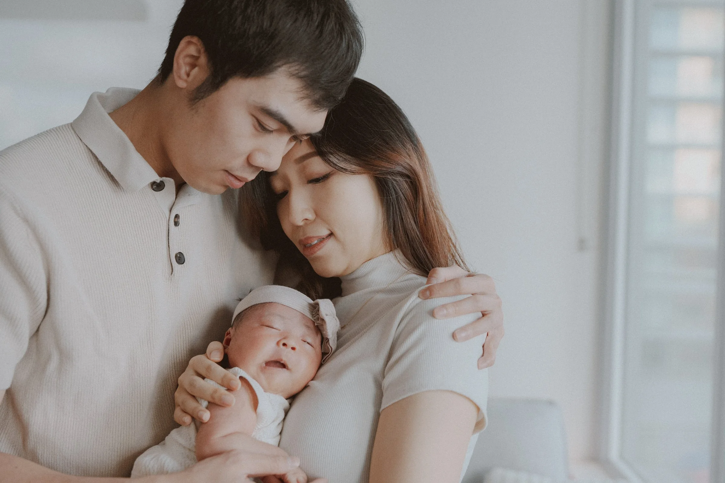 Close-up of parents resting their heads together while holding their baby.