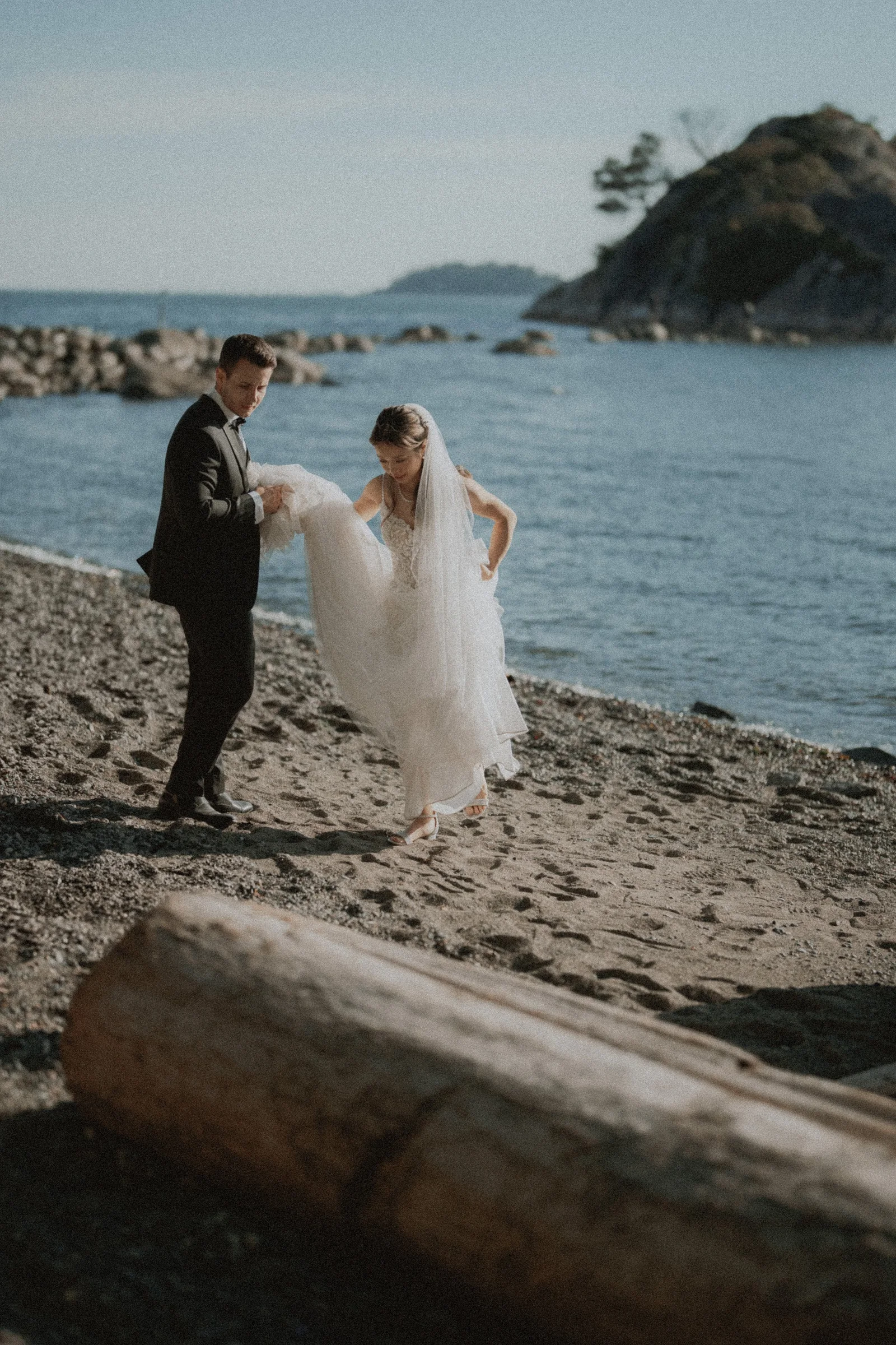 Bride and groom stepping across the beach with a rocky island behind them.