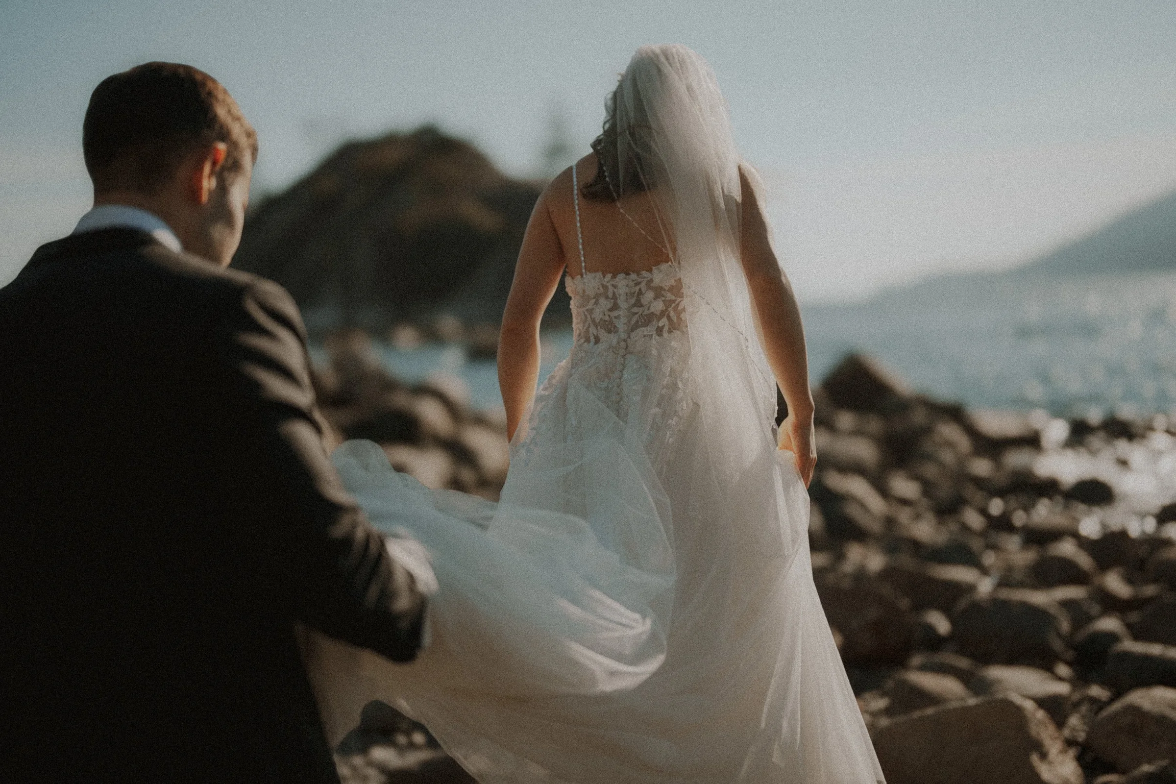 View from behind the couple as they cross the pebbled shoreline.