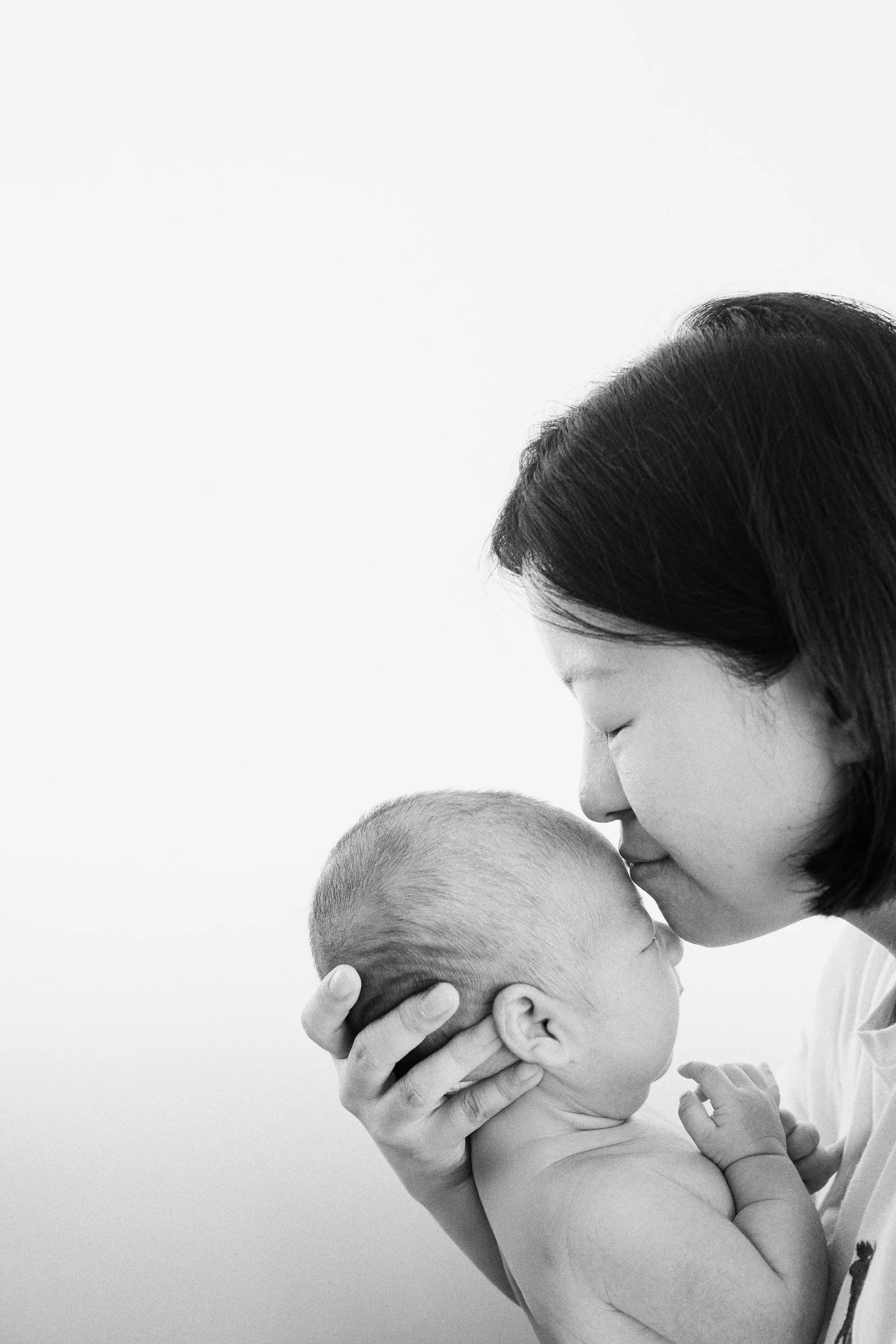 Mother kissing newborn baby Apollo on the forehead, intimate black and white portrait.