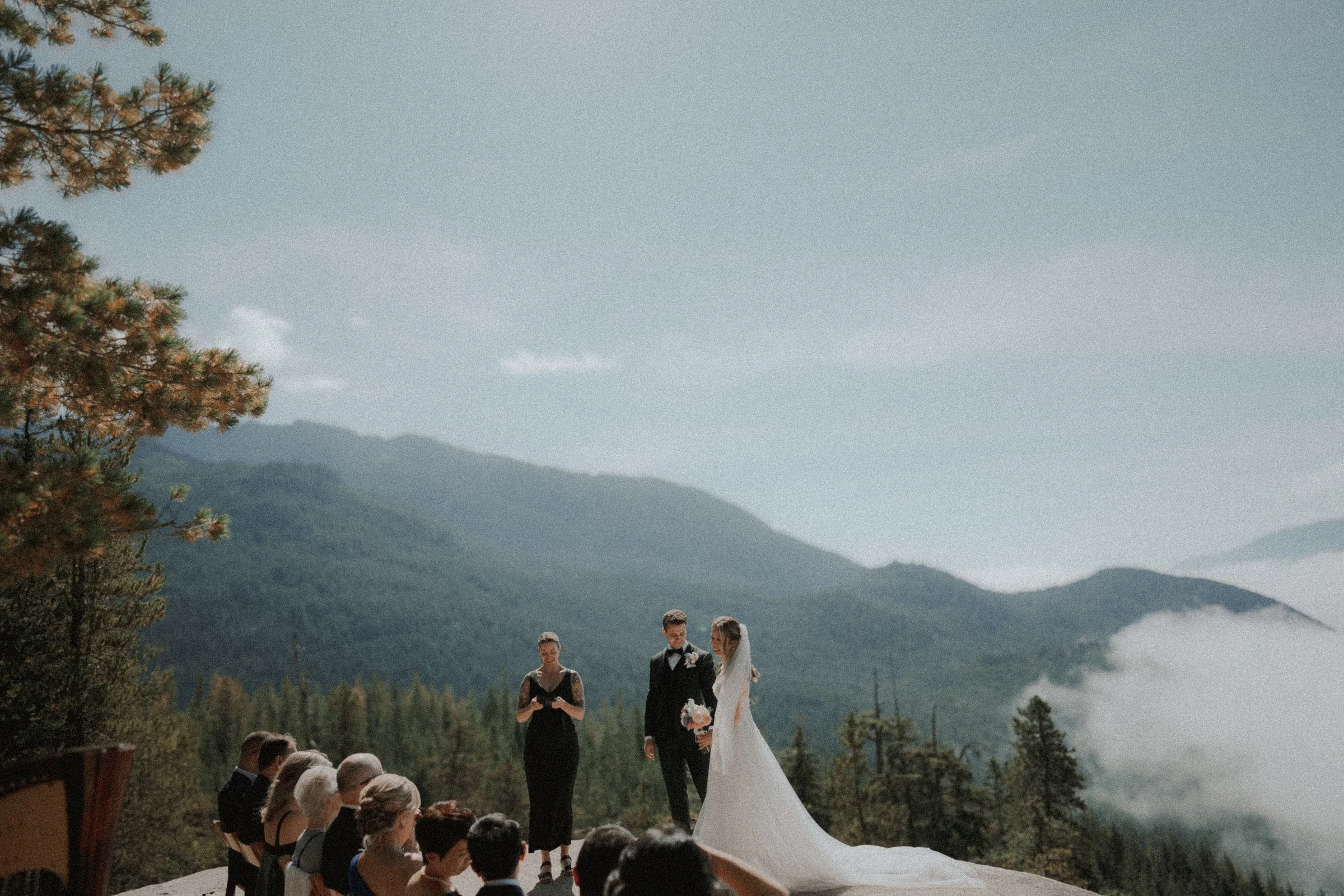 Wedding guests watching the mountain ceremony from wooden chairs.