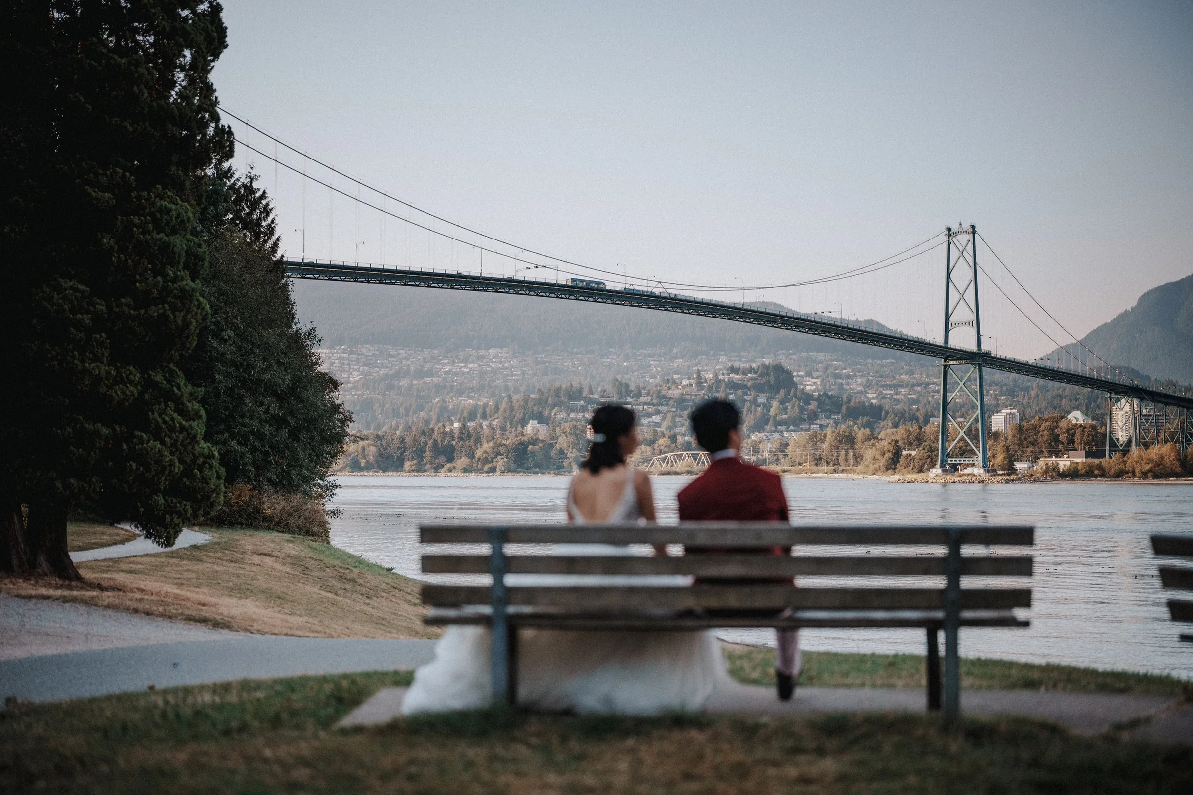 Couple seated on a waterfront bench overlooking Lions Gate Bridge.
