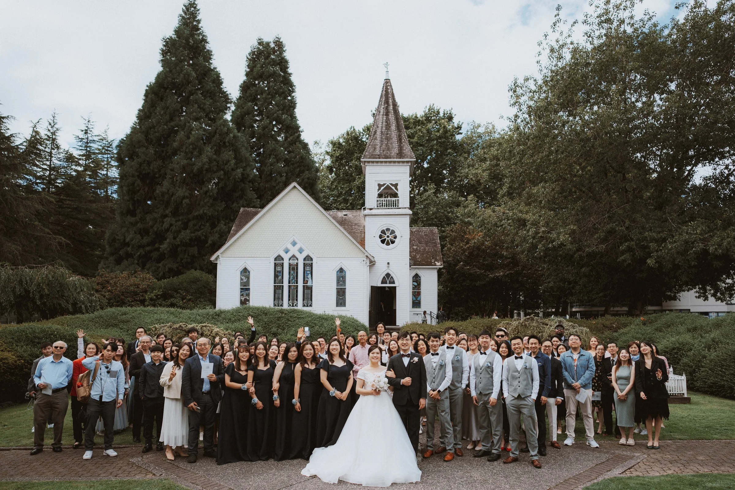 Wedding guests and newlyweds posing beneath Minoru Chapel's white tower.