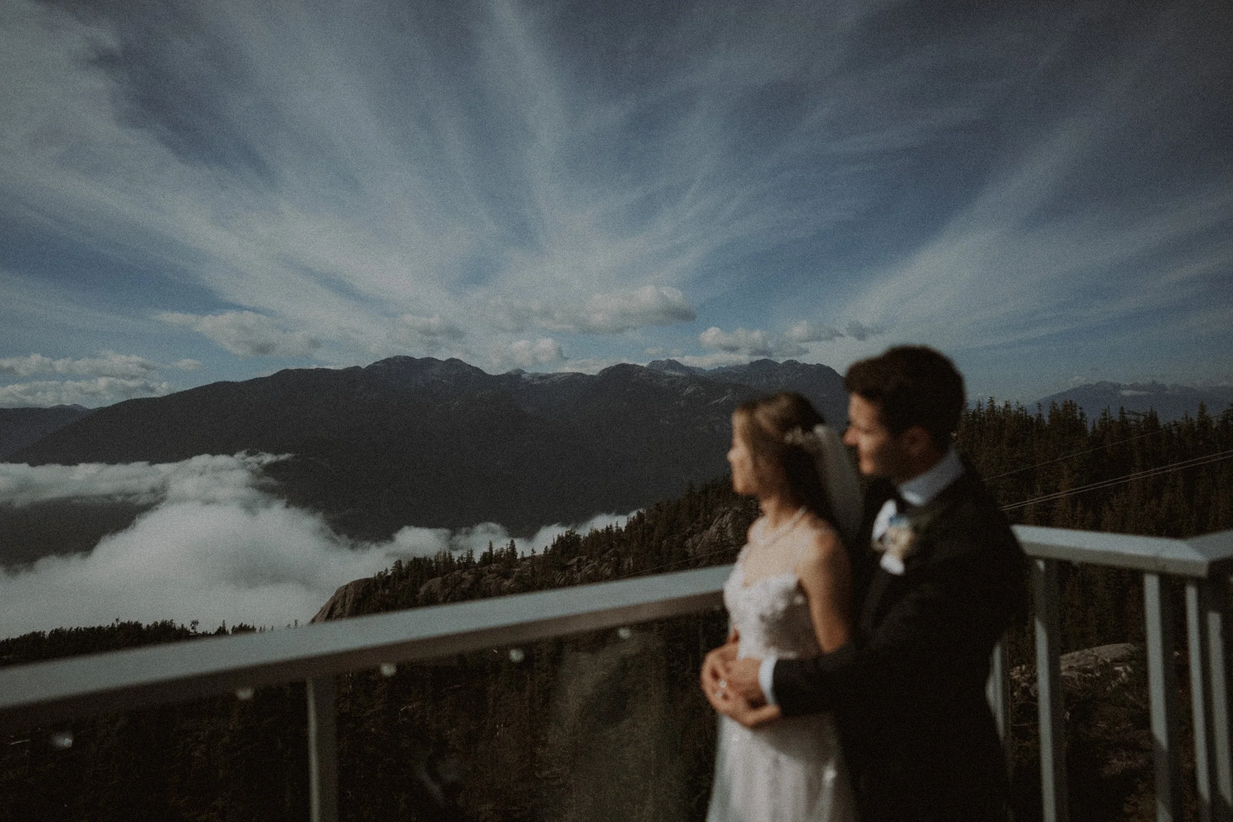 Bride and groom leaning together on a viewing deck above the cloud layer.