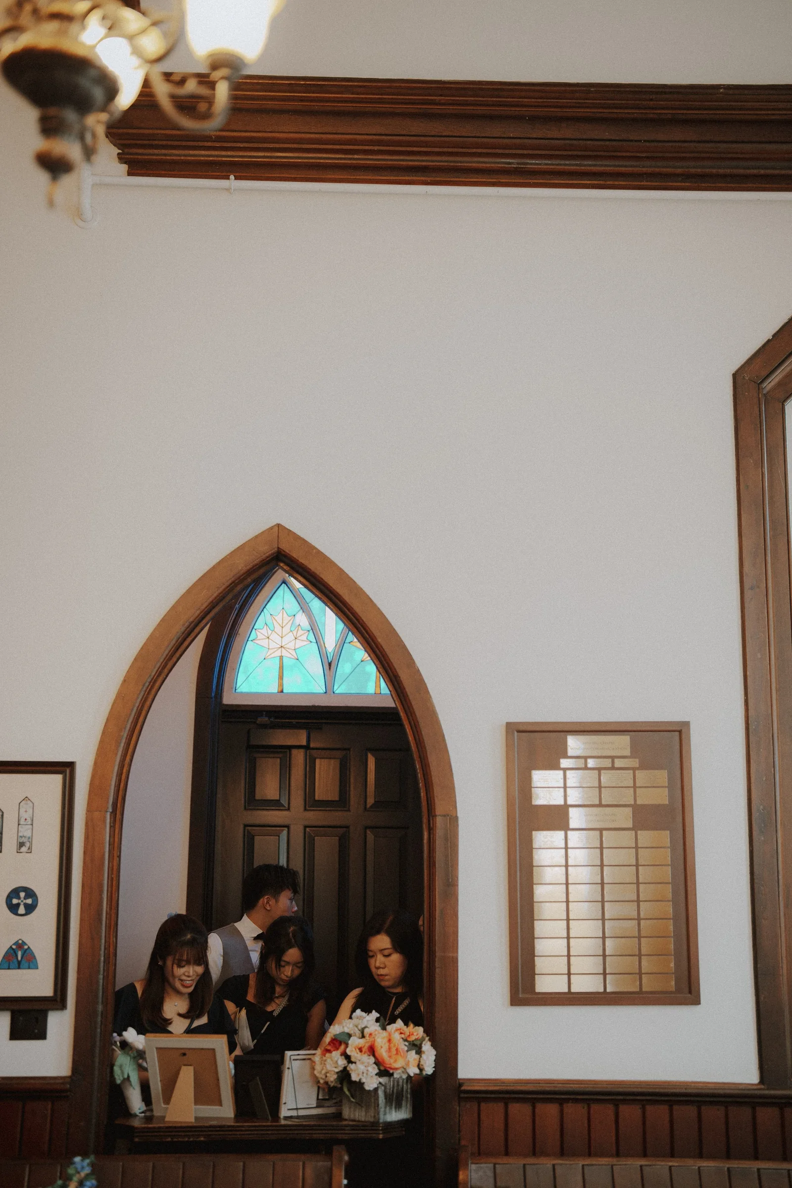 Wedding party gathered beside a pointed wooden doorway inside Minoru Chapel.