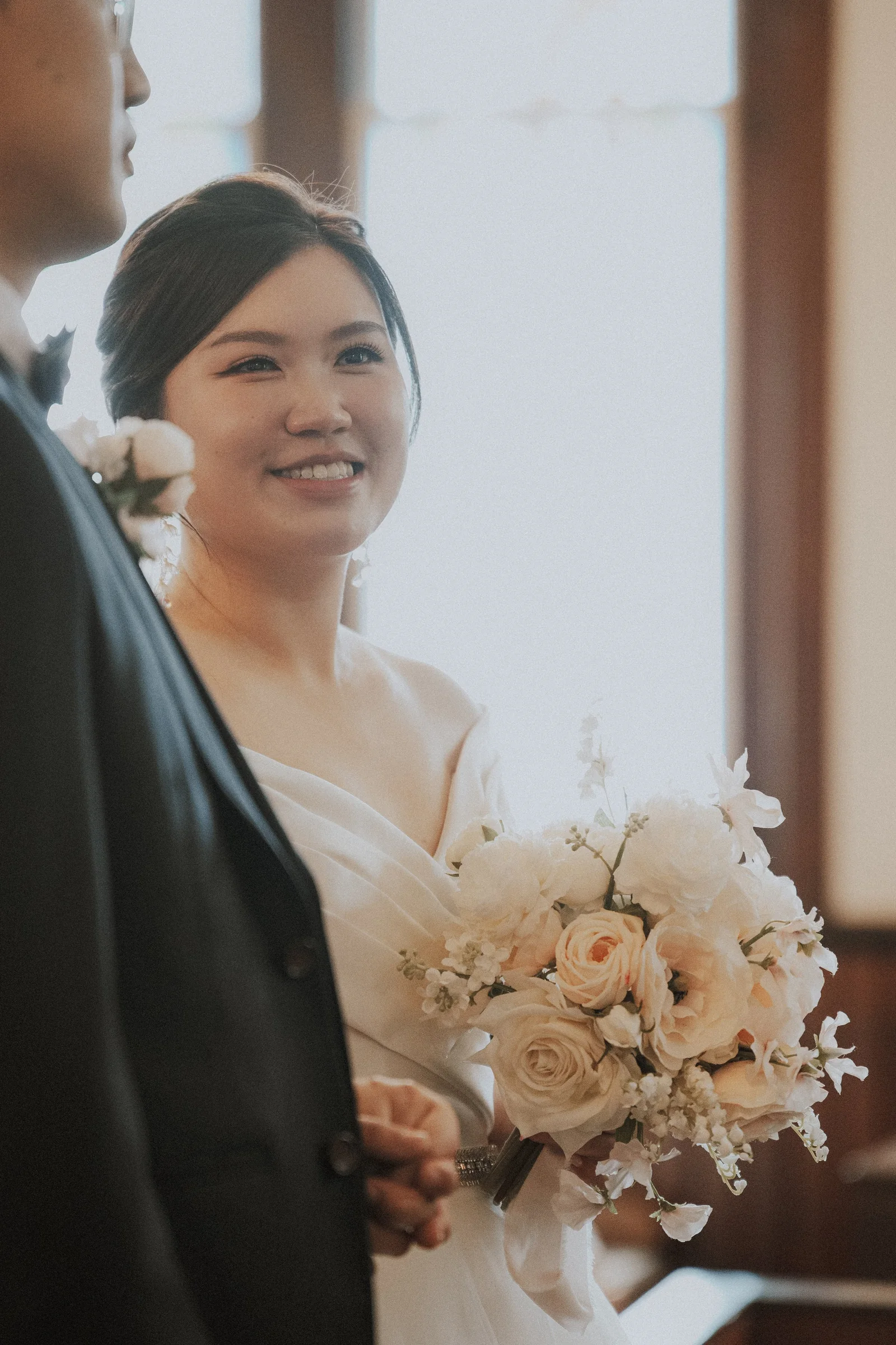 Smiling bride holding her bouquet as she faces the groom.