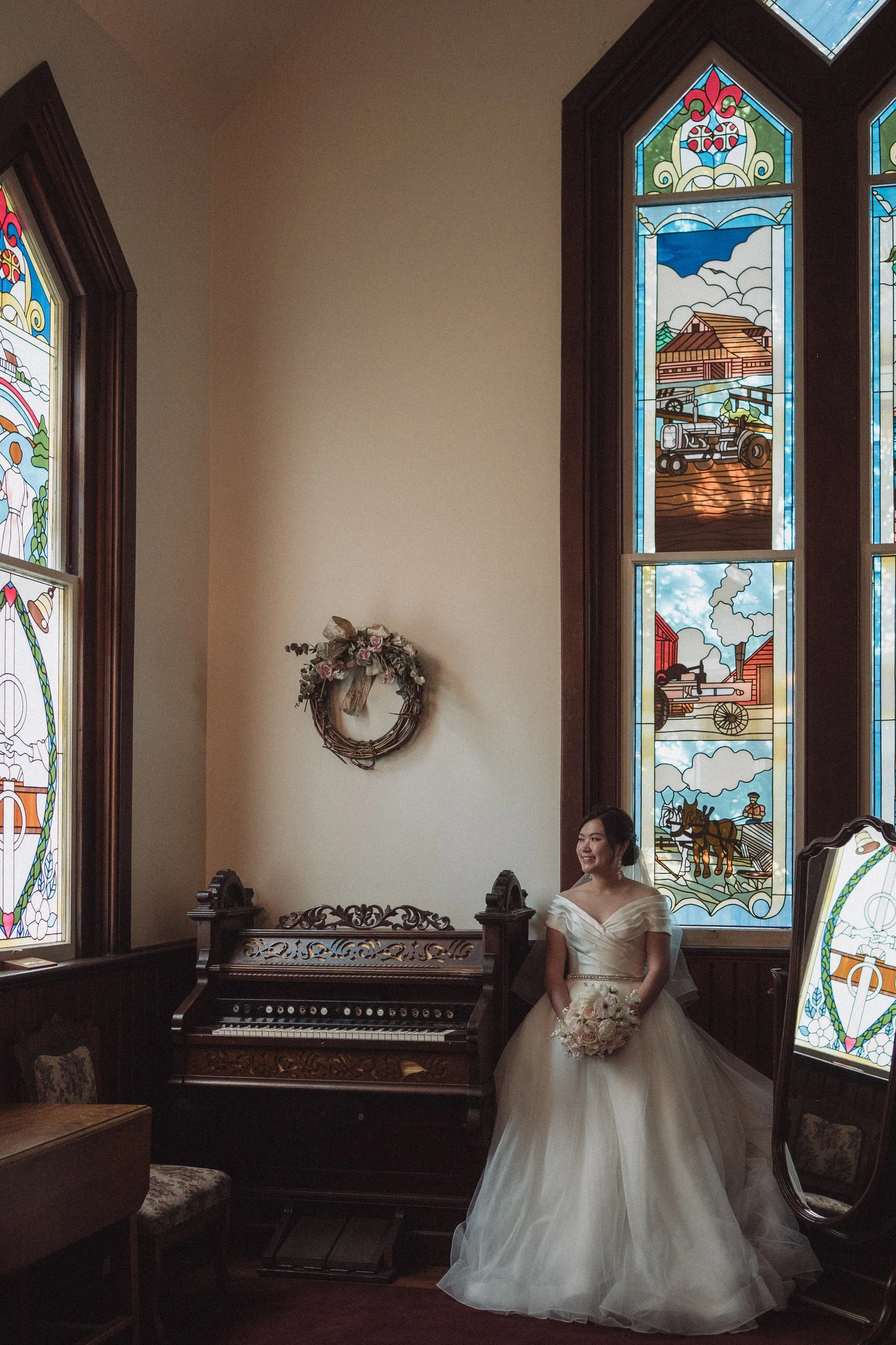 Bride standing beside tall stained-glass windows with her bouquet.