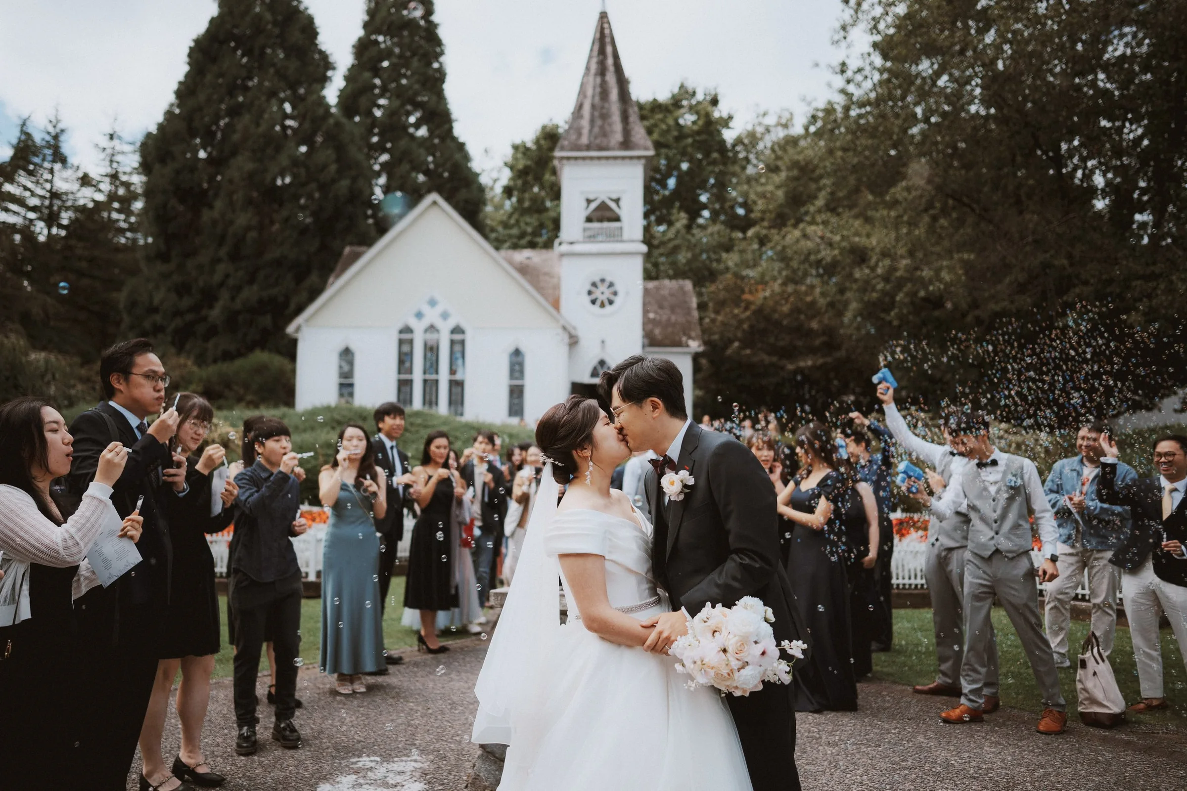 Couple kissing on the path outside Minoru Chapel as guests celebrate.